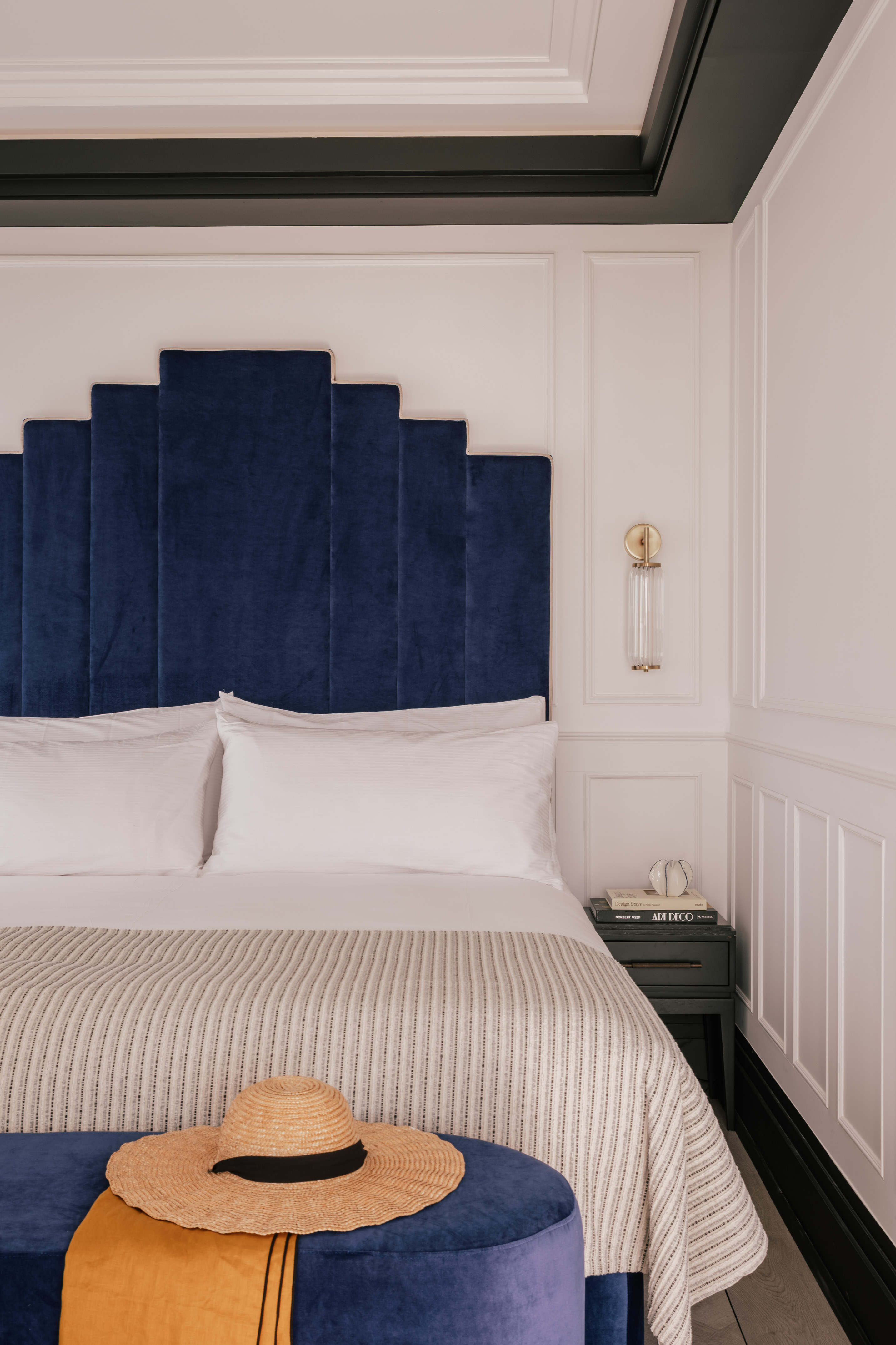 Blue velvet geometric headboard, white bed, striped blanket, nightstand in bedroom.