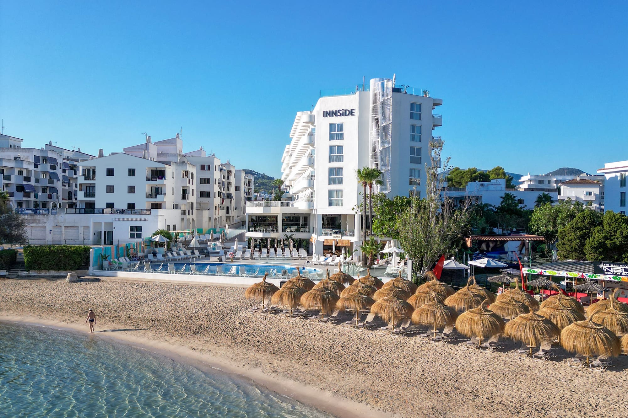 White INNSiDE hotel, sandy beach, straw umbrellas, and clear blue ocean.