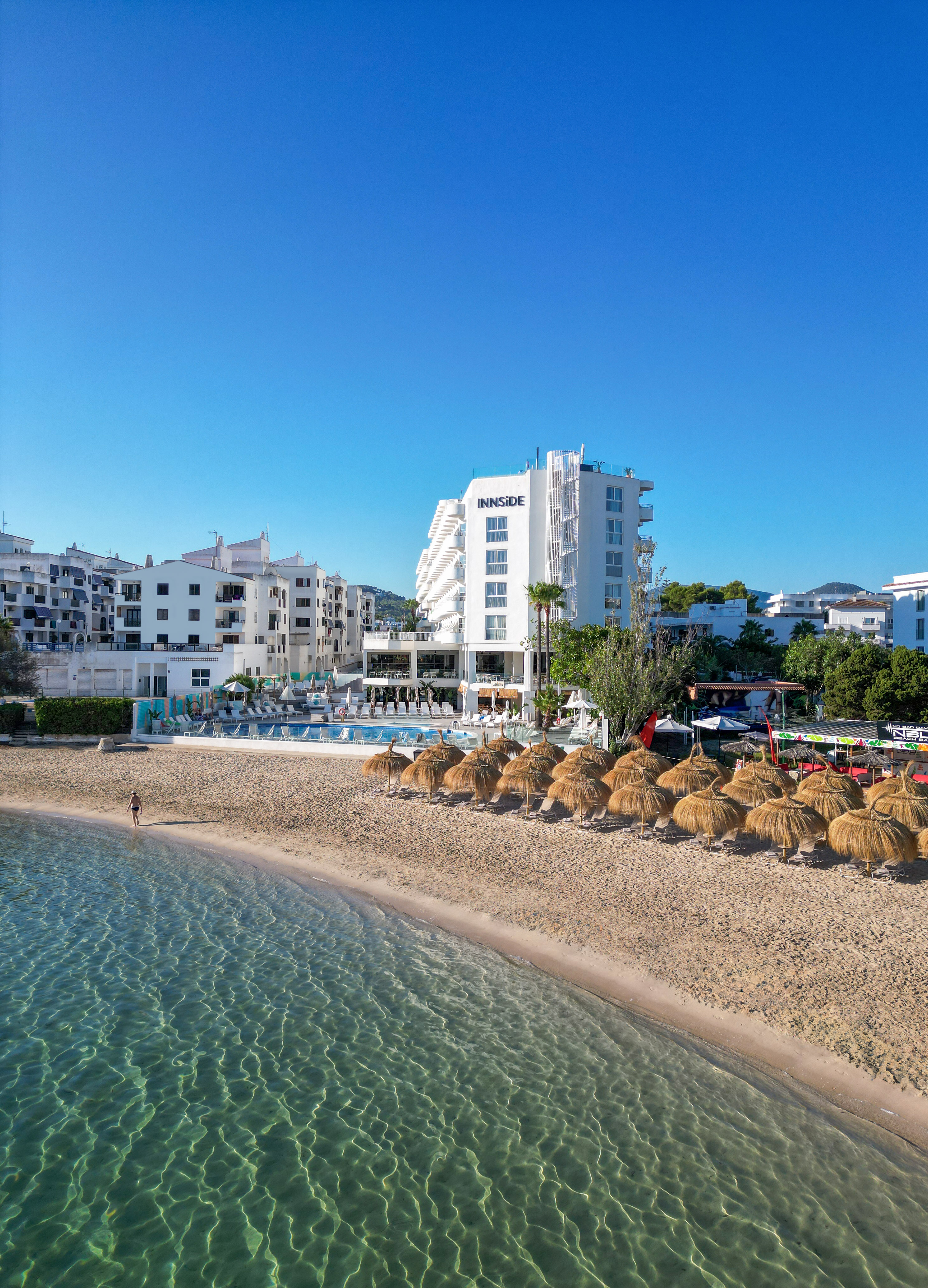 White INNSiDE hotel, sandy beach, straw umbrellas, and clear blue ocean.