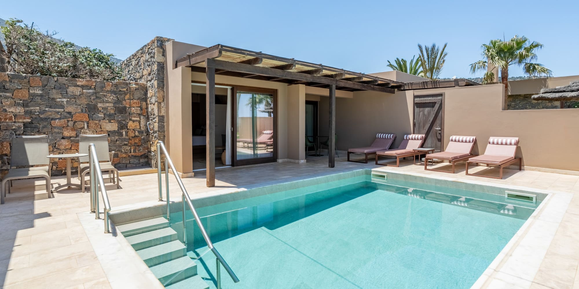 Private pool suite with sun loungers, shaded patio, and stone wall.