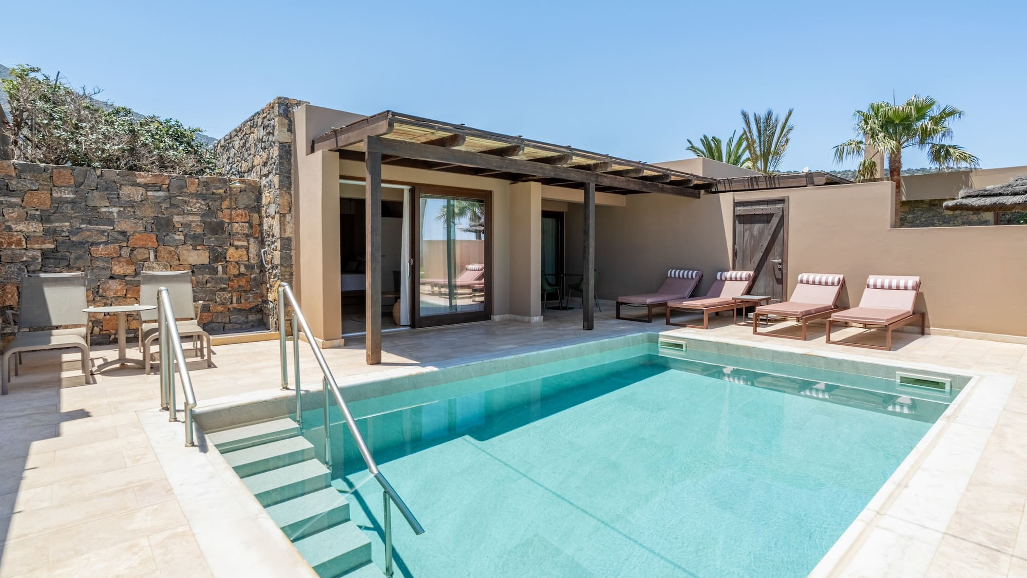 Private pool suite with sun loungers, outdoor patio, and stone wall.