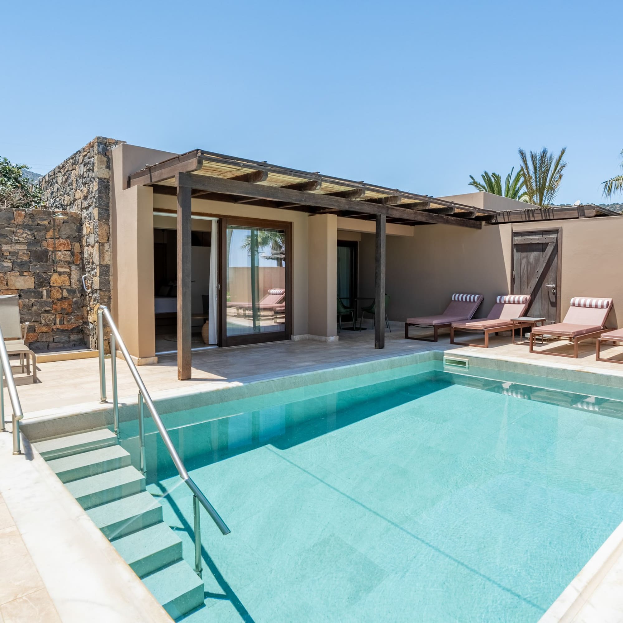 Private pool suite with sun loungers, outdoor patio, and stone wall.