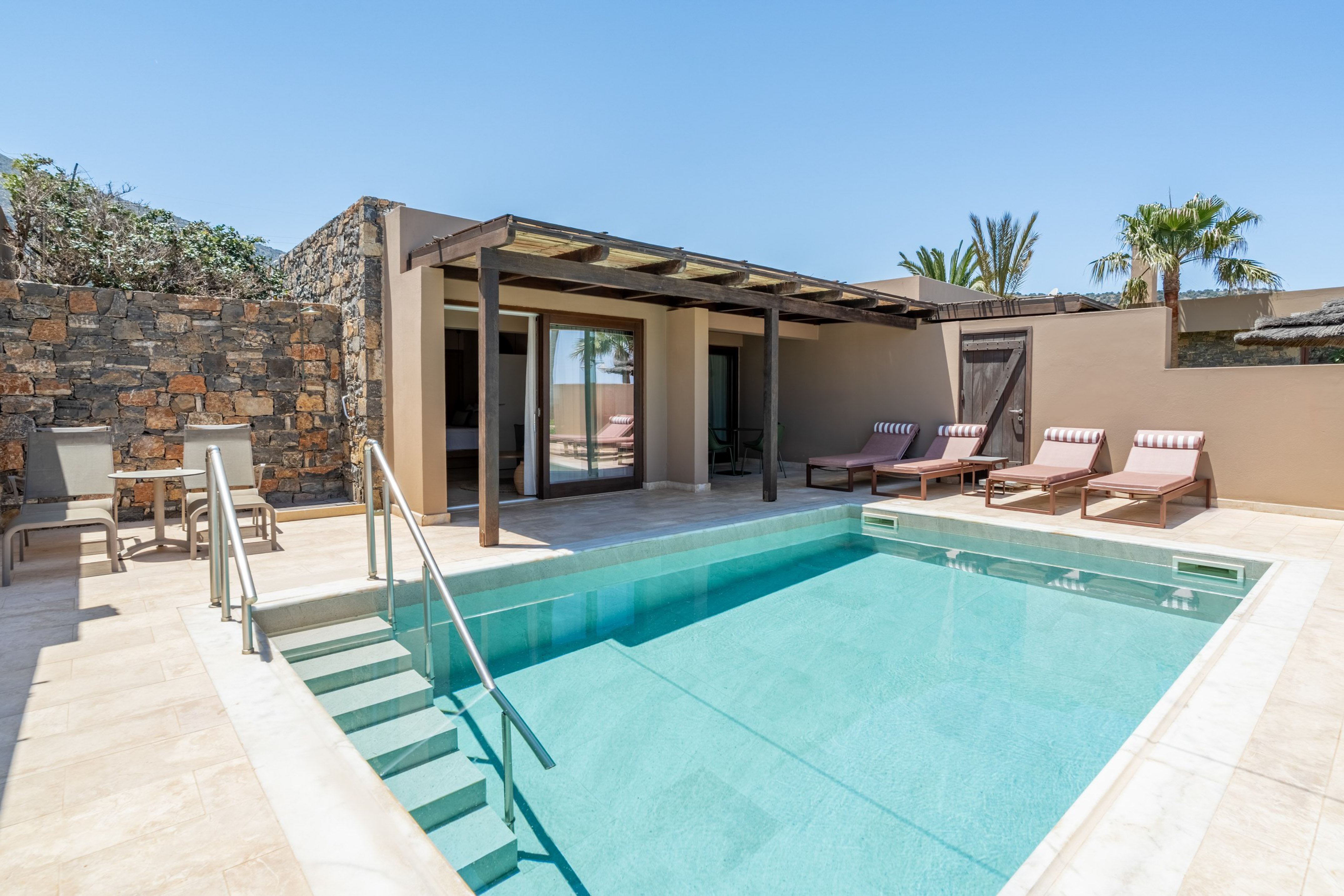 Private pool suite with sun loungers, outdoor patio, and stone wall.