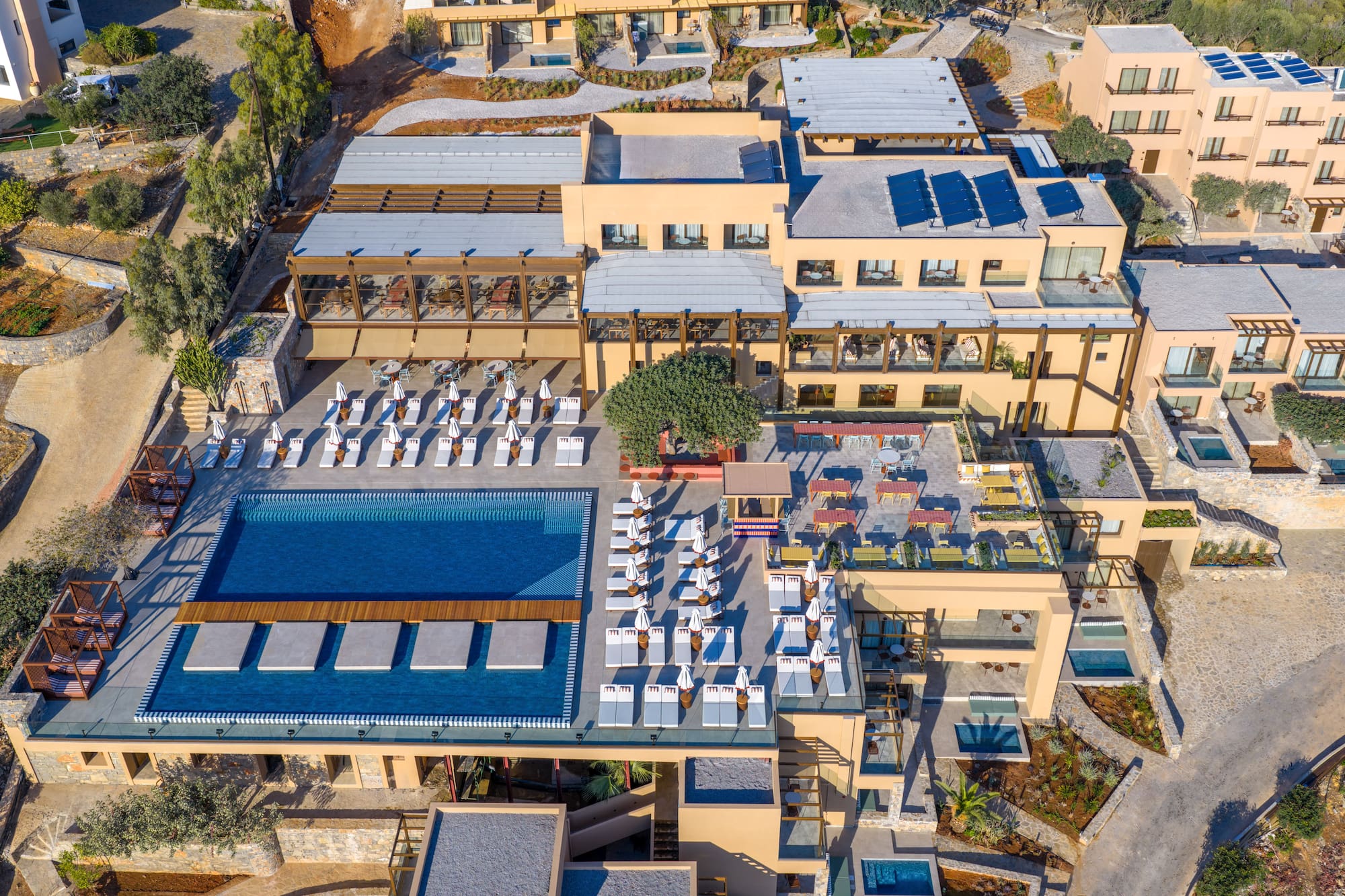 Luxury resort aerial: large pool, private pools, sun loungers, solar panels.