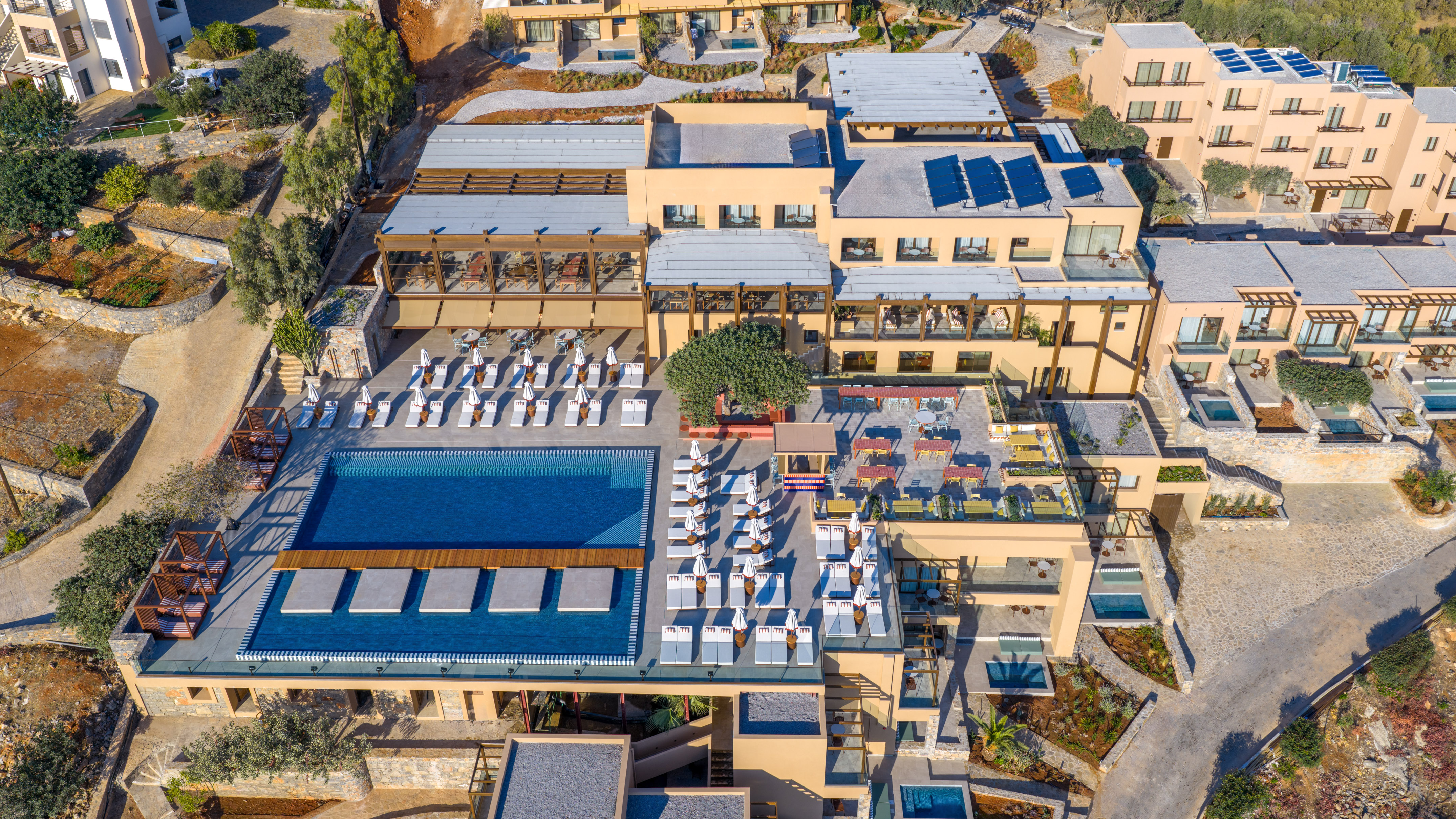 Luxury resort aerial: large pool, private pools, sun loungers, solar panels.