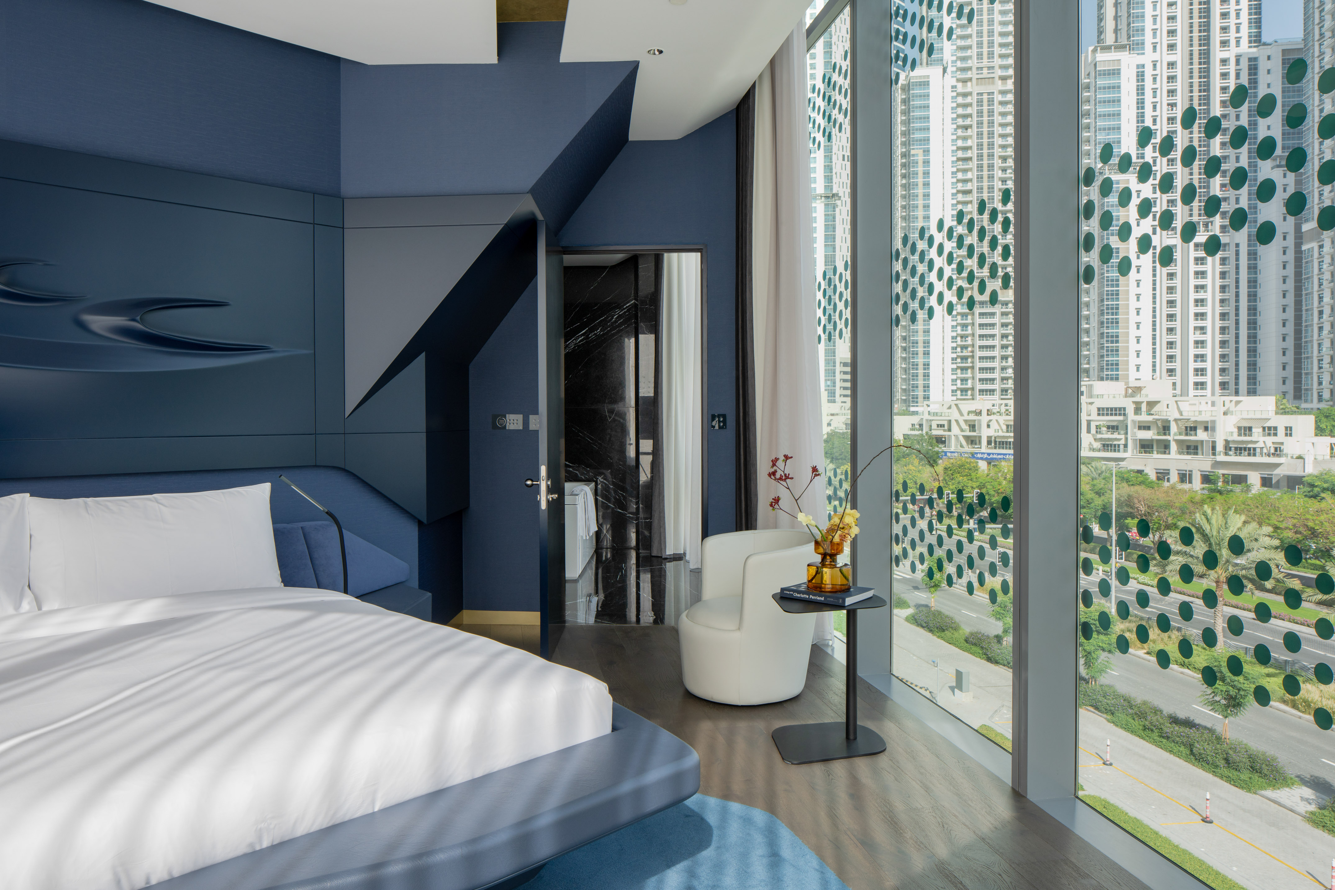 Modern blue bedroom with cityscape view, white bed, and sleek design.