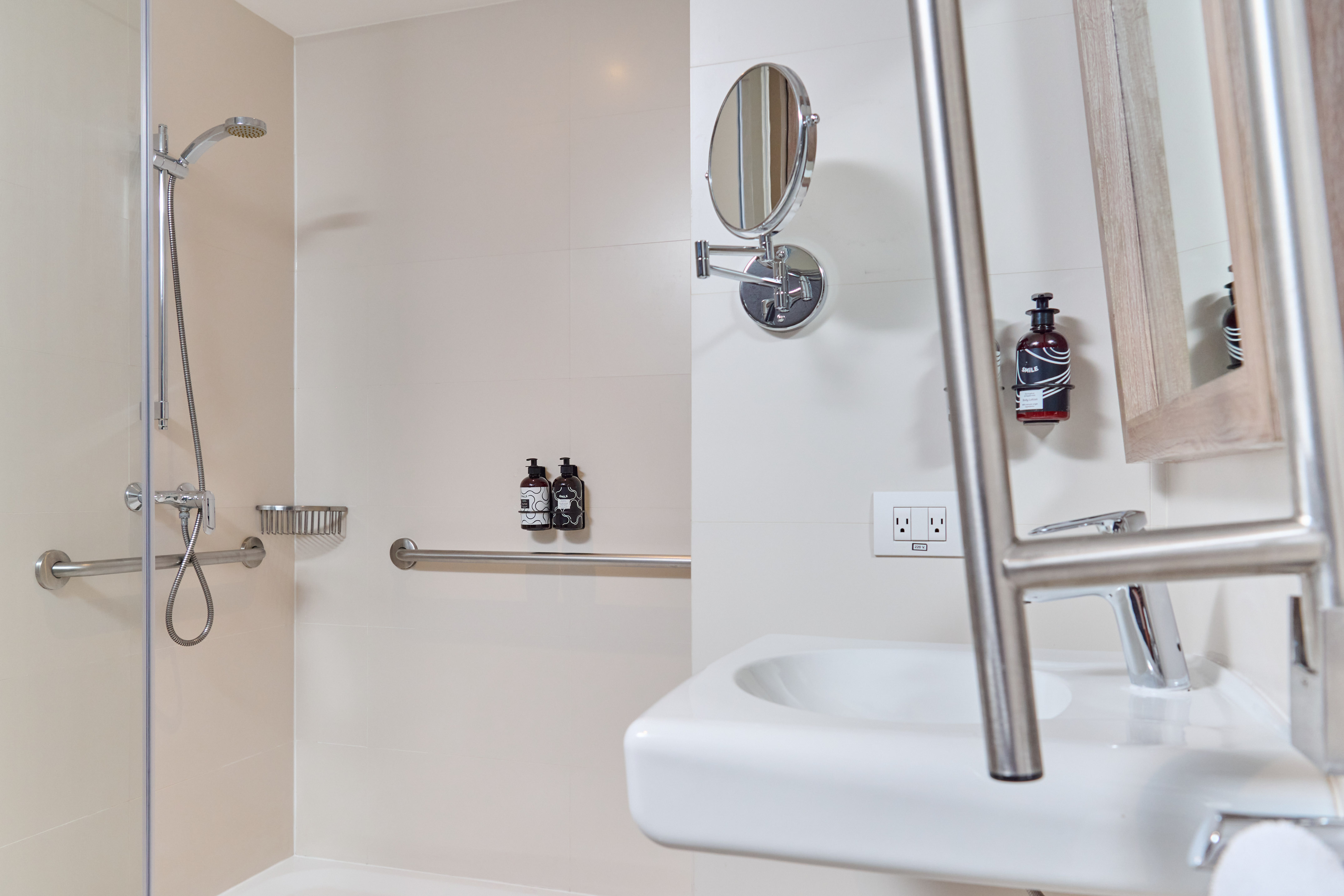 Clean, modern hotel bathroom with shower, sink, and accessible grab bars.