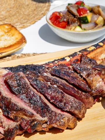 a large piece of meat on a cutting board with a bowl of salad