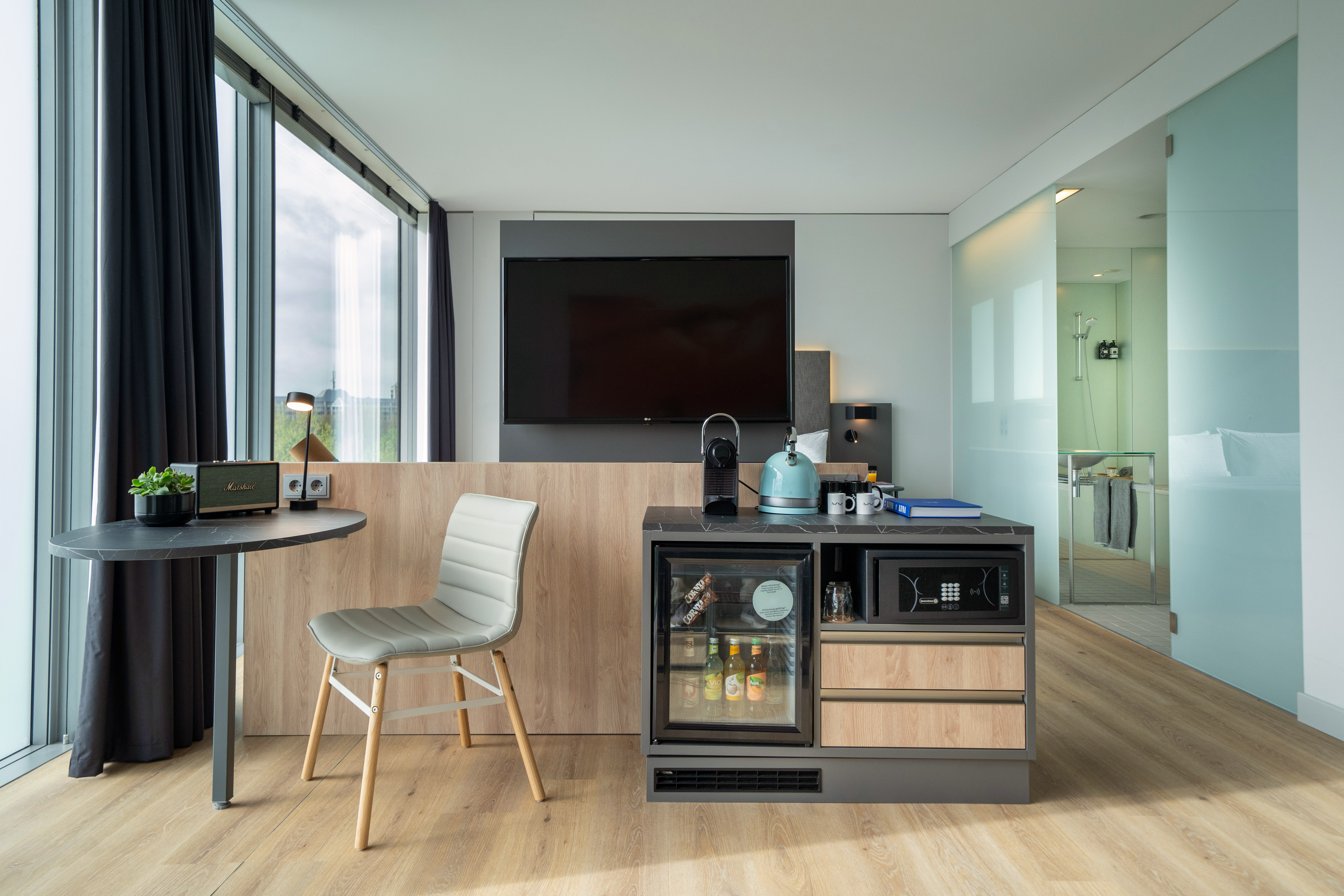 Modern hotel suite with large TV, Nespresso, minibar, and work desk.
