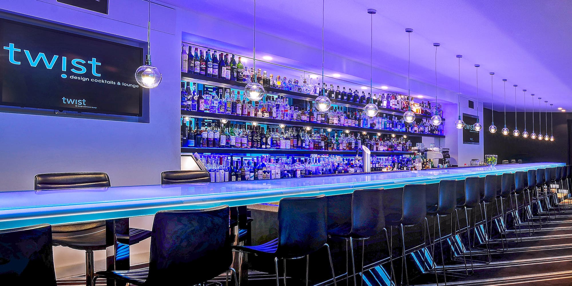 a bar with a row of chairs and a shelf with bottles