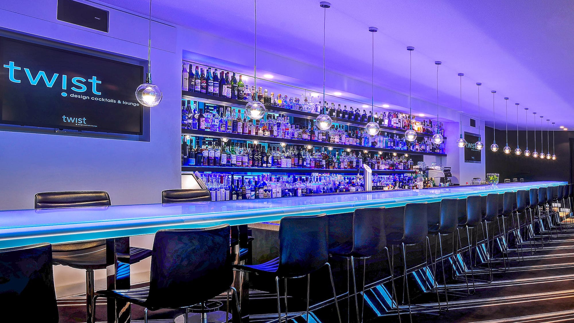 a bar with a row of chairs and a shelf with bottles