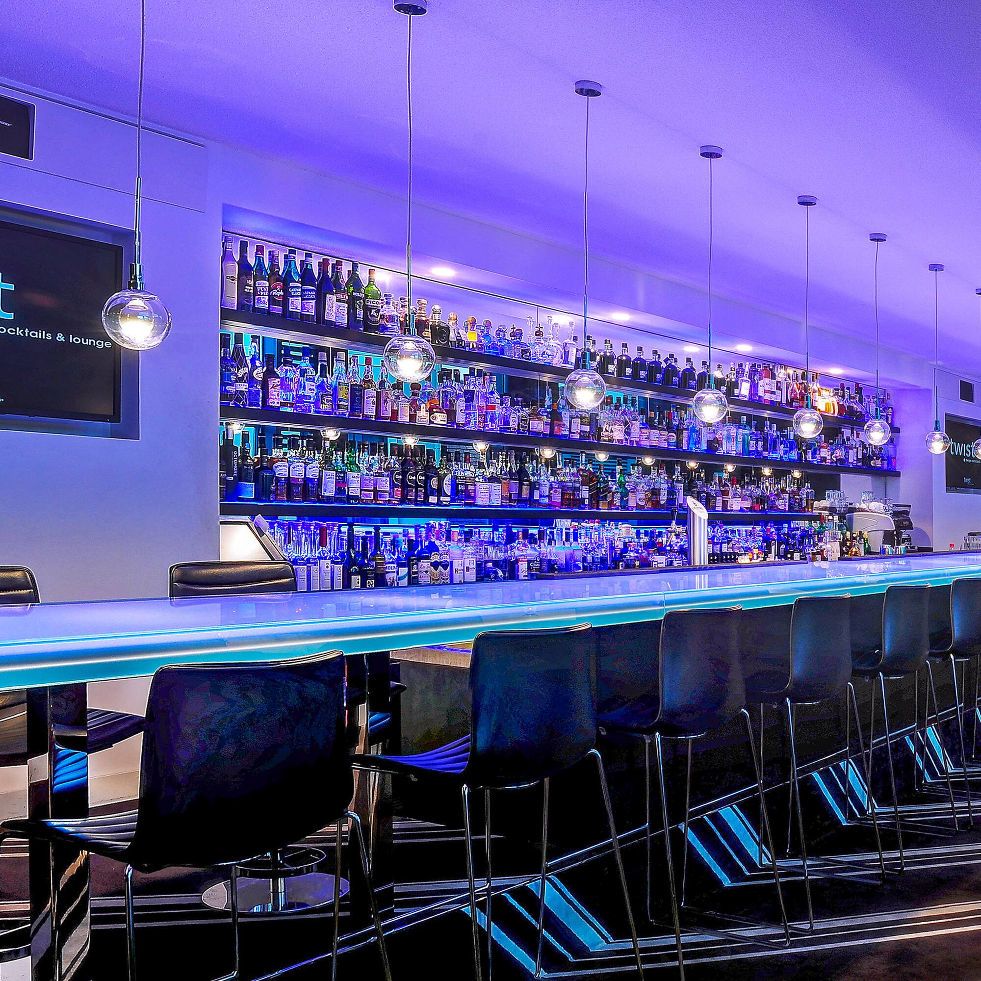 a bar with a row of chairs and a shelf with bottles