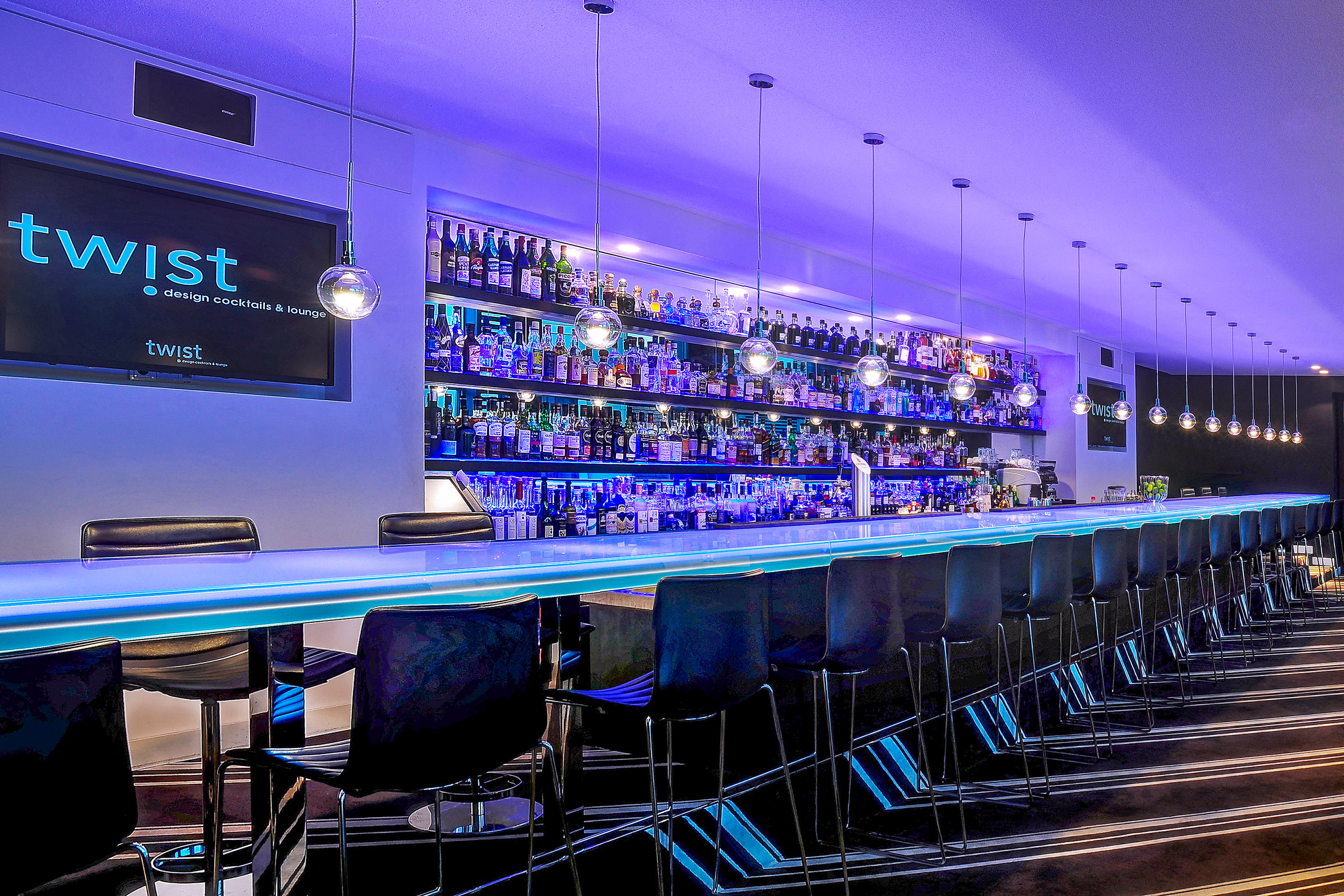 a bar with a row of chairs and a shelf with bottles