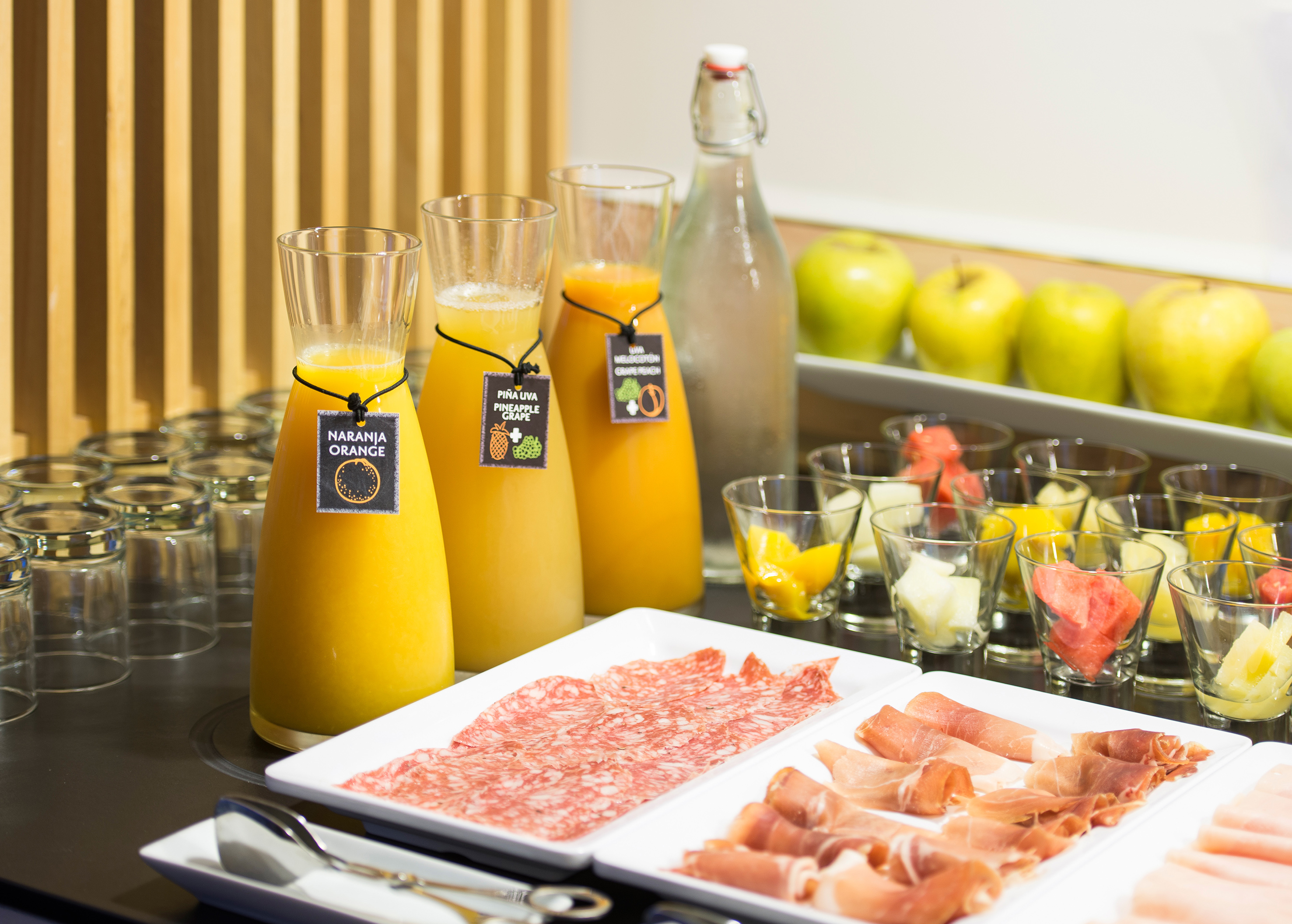 Breakfast buffet with fresh orange juice, cold cuts, fruit, and green apples.