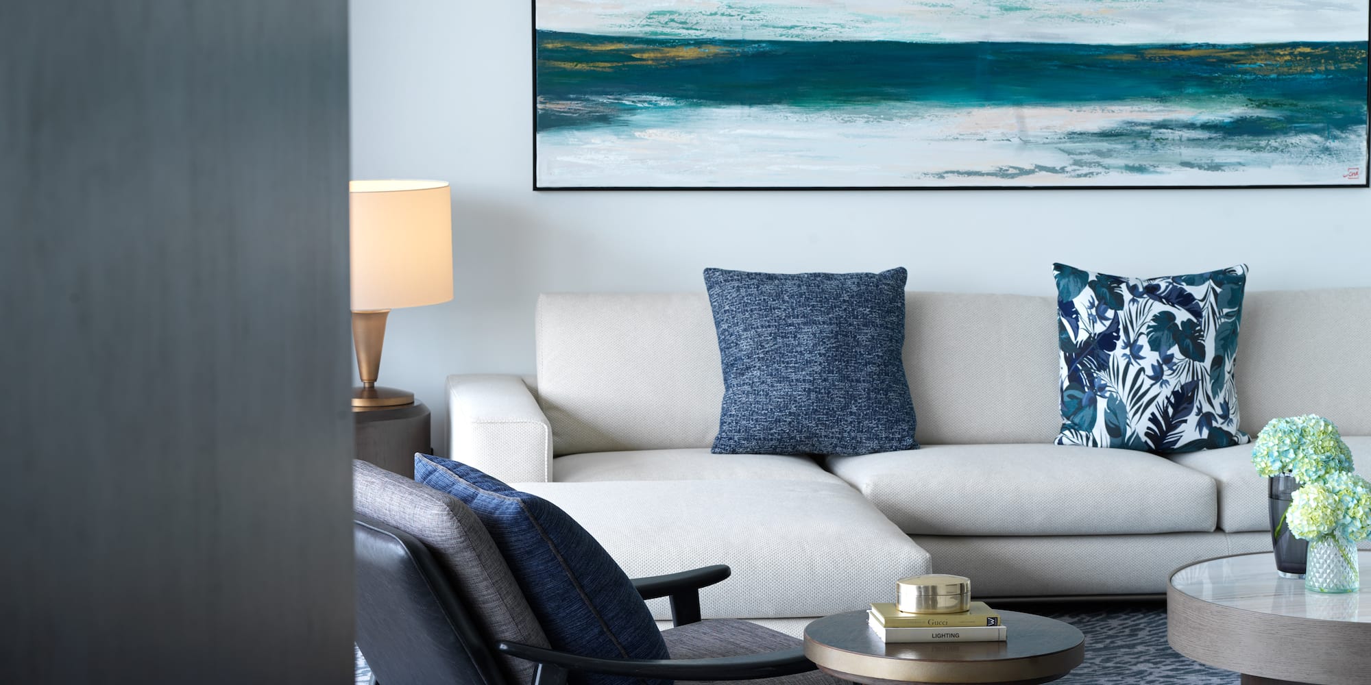 a white couch with blue pillows and a painting on the wall