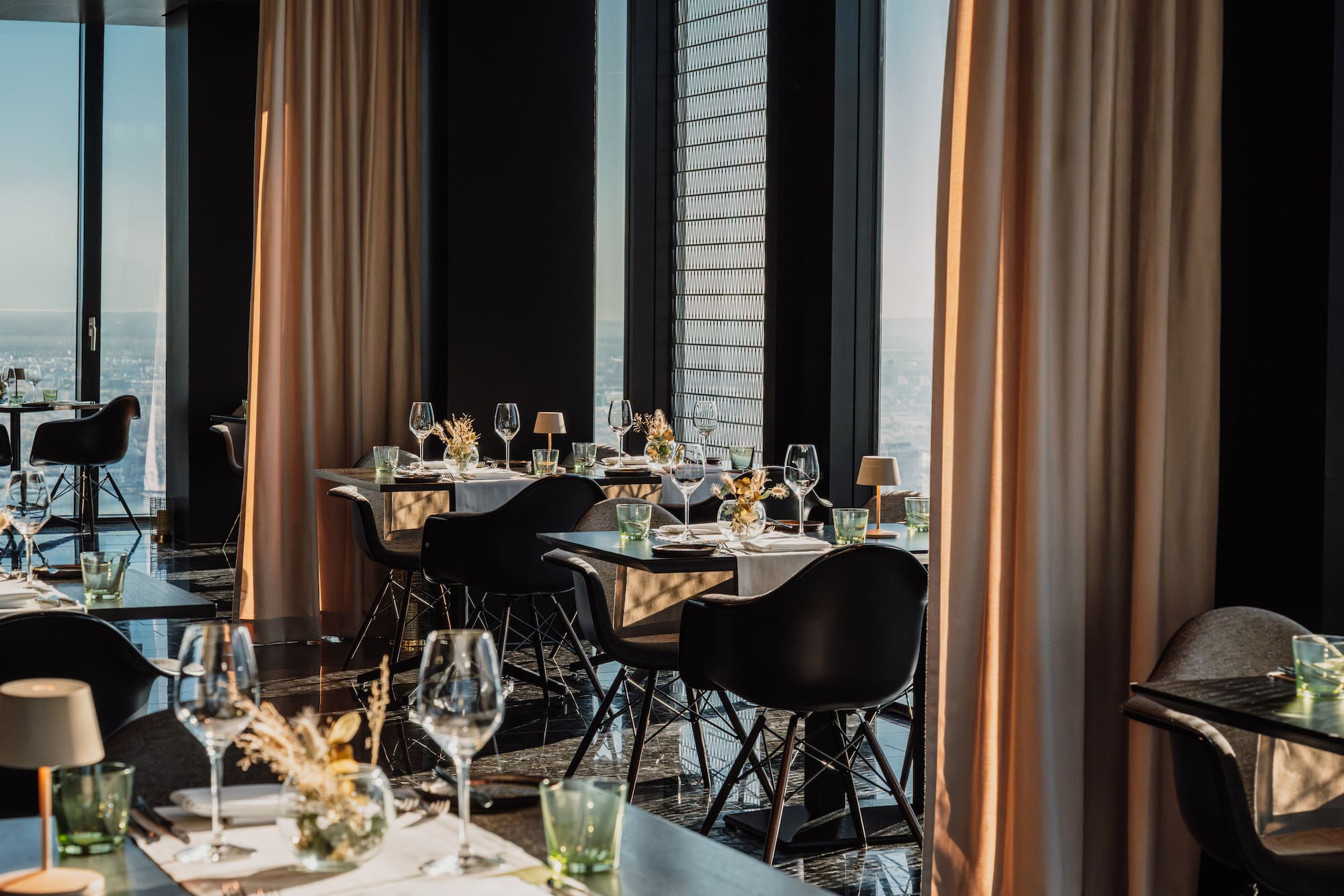 Luxury restaurant interior with set tables, city skyline view, and modern decor.