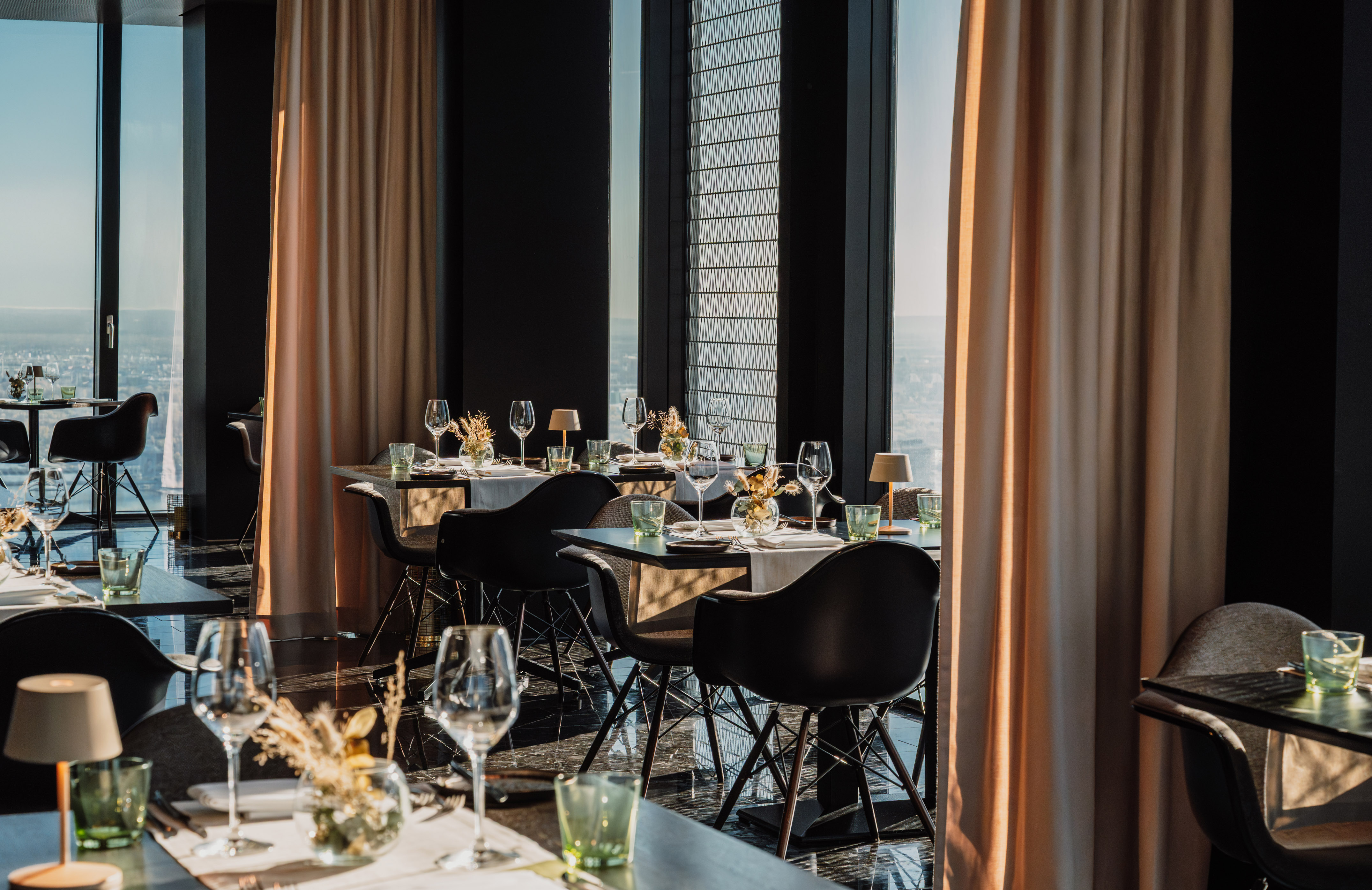 Luxury restaurant interior with set tables, city skyline view, and modern decor.