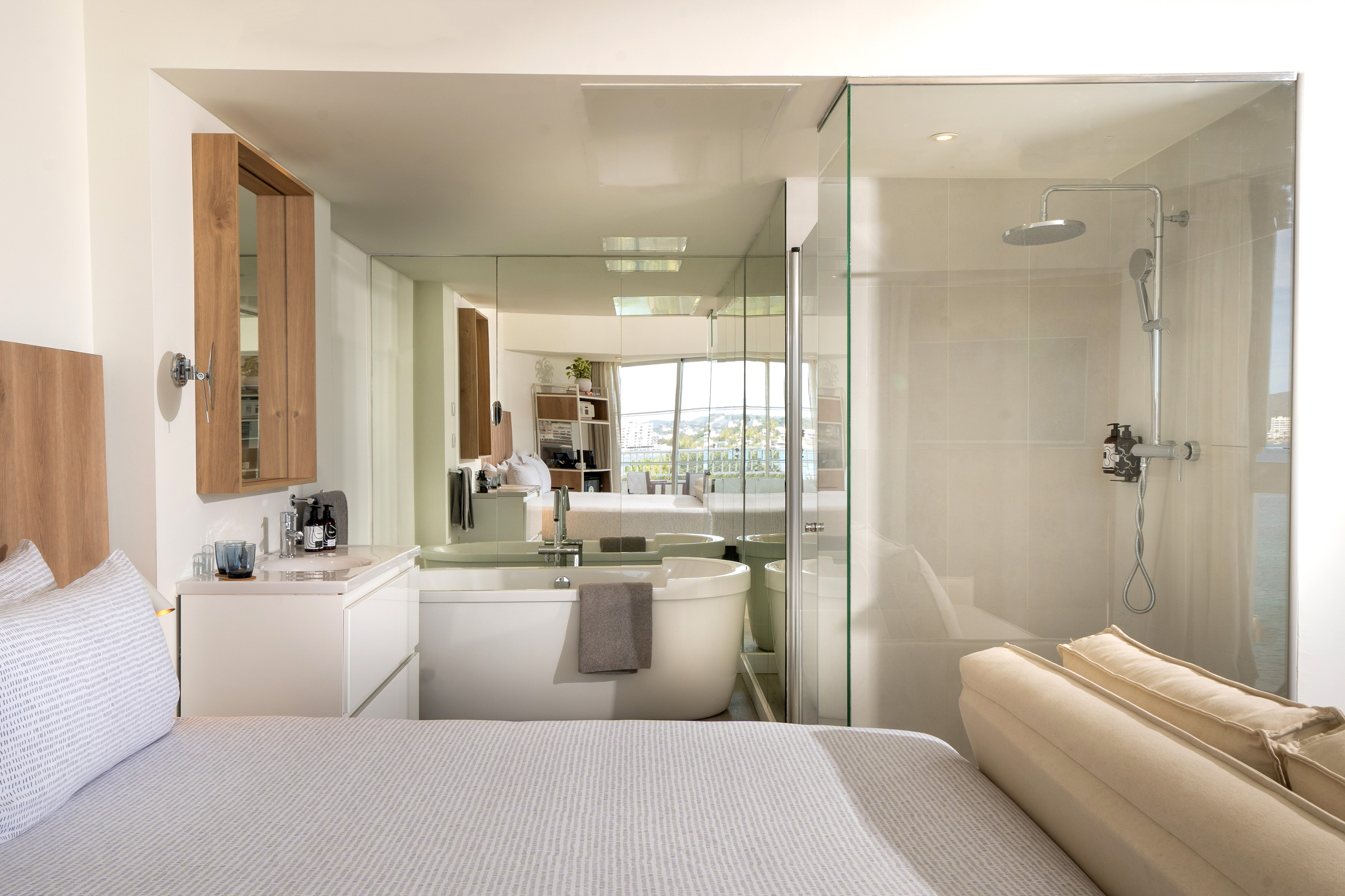 Hotel room with open-plan bathroom, soaking tub, and glass shower.