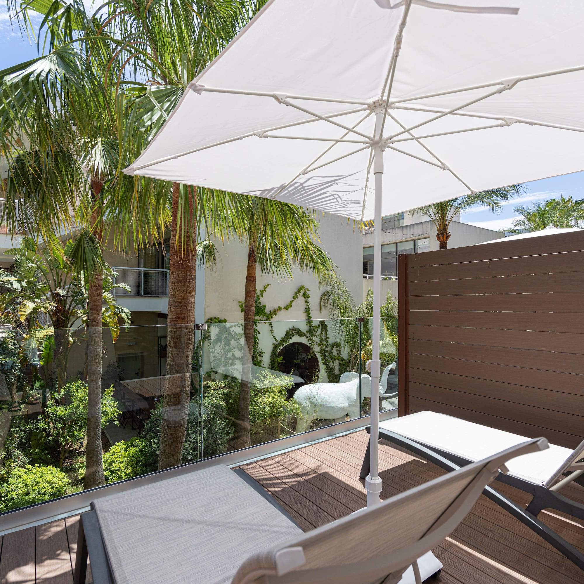 Relaxing balcony with lounge chairs, white umbrella, and tropical palm trees.
