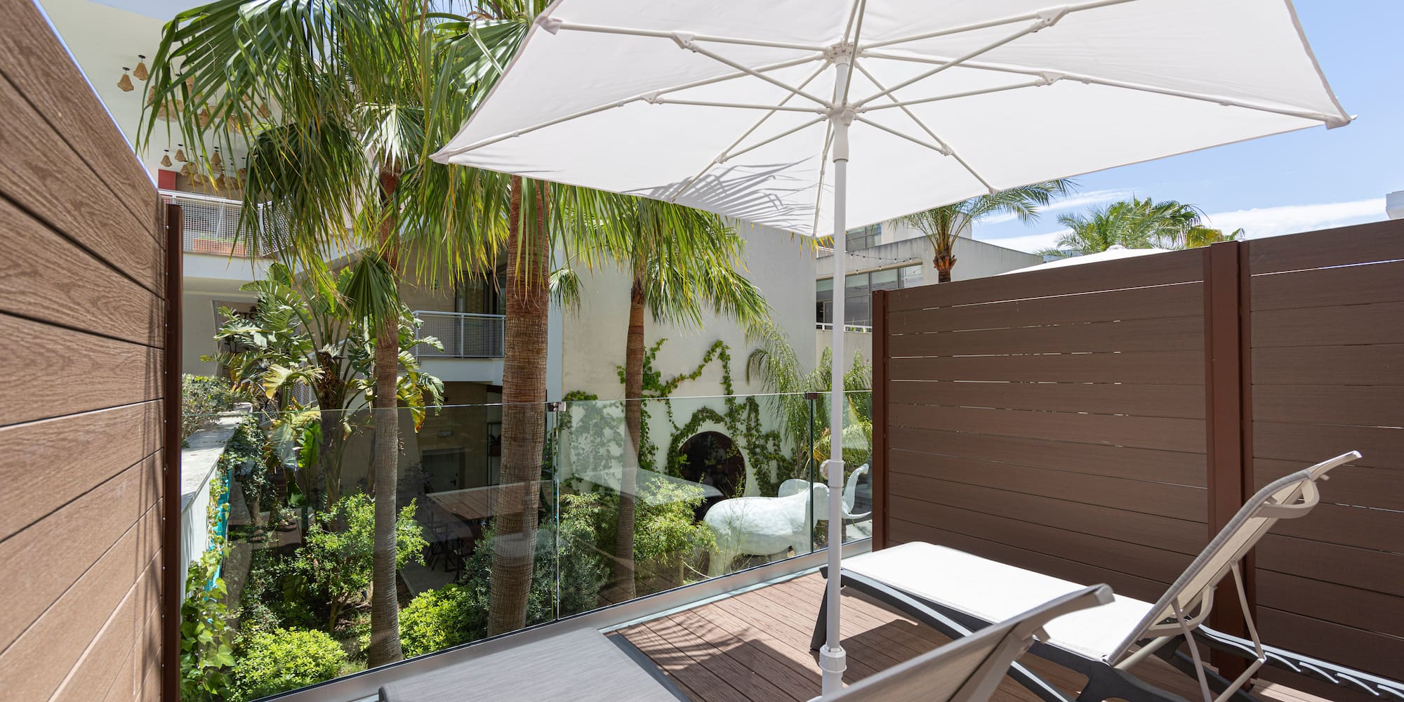 Relaxing balcony with lounge chairs, white umbrella, and tropical palm trees.