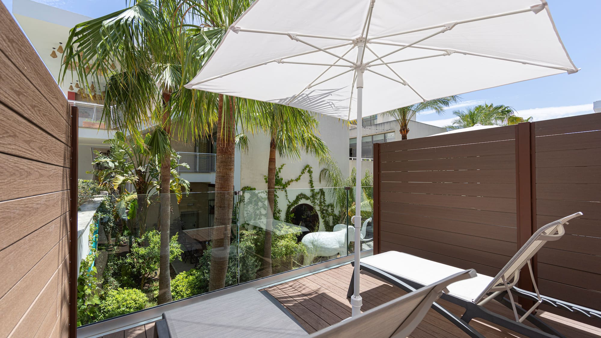 Relaxing balcony with lounge chairs, white umbrella, and tropical palm trees.