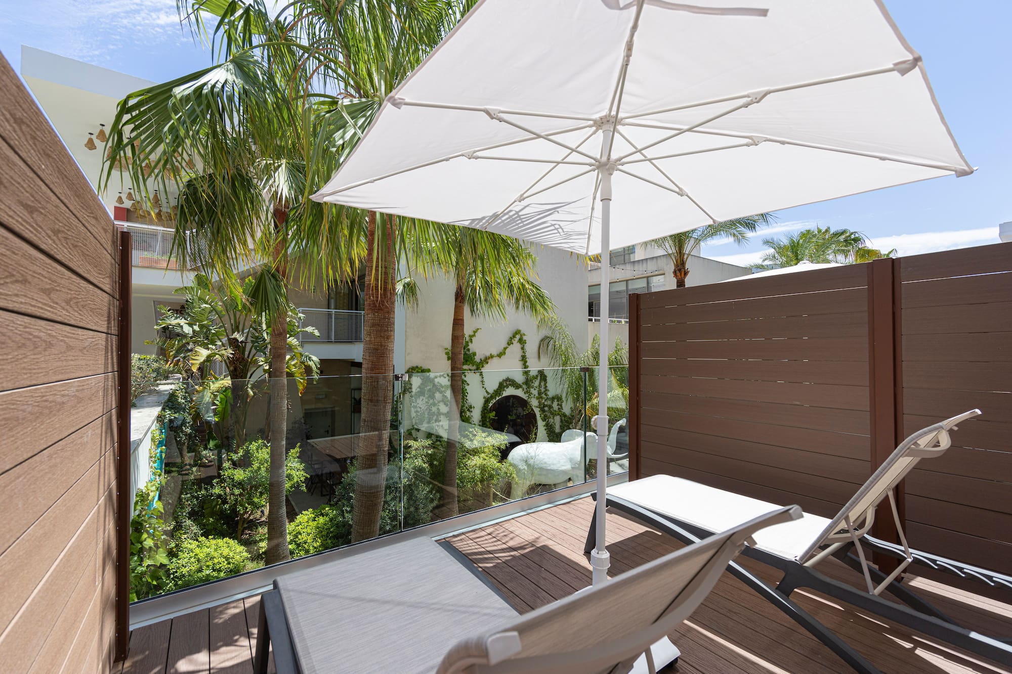 Relaxing balcony with lounge chairs, white umbrella, and tropical palm trees.