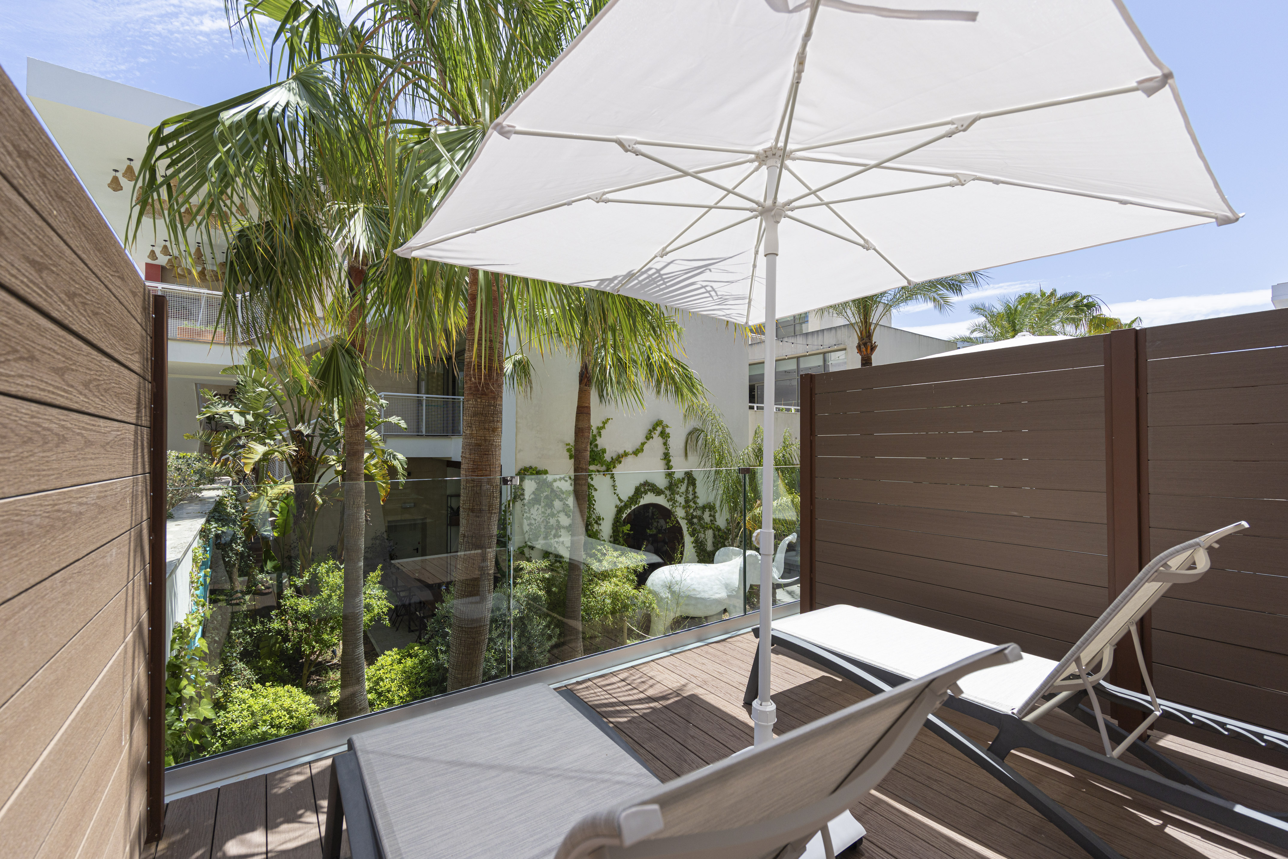 Relaxing balcony with lounge chairs, white umbrella, and tropical palm trees.