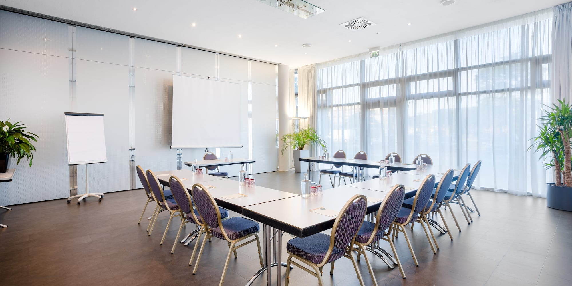 Modern U-shaped conference room setup with projection screens, large windows.
