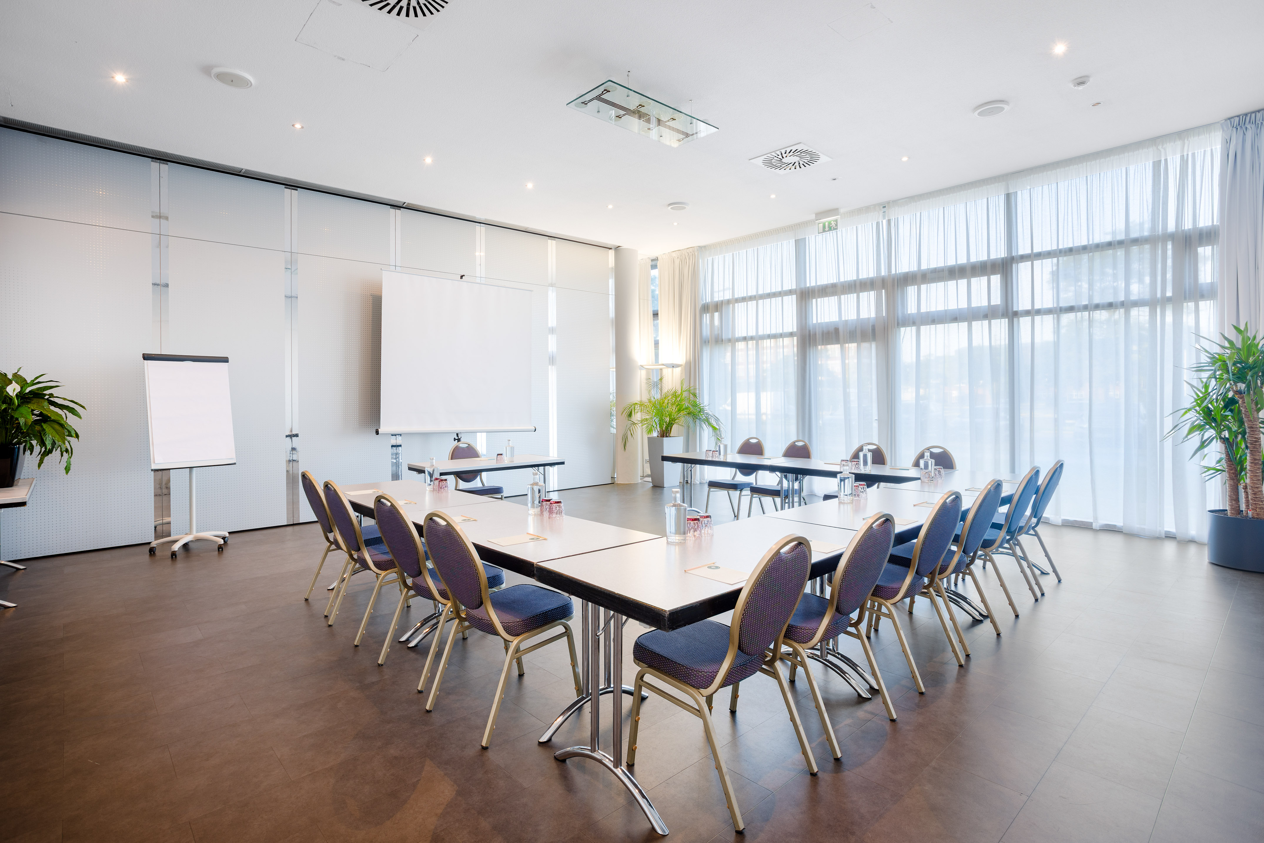 Modern U-shaped conference room setup with projection screens, large windows.