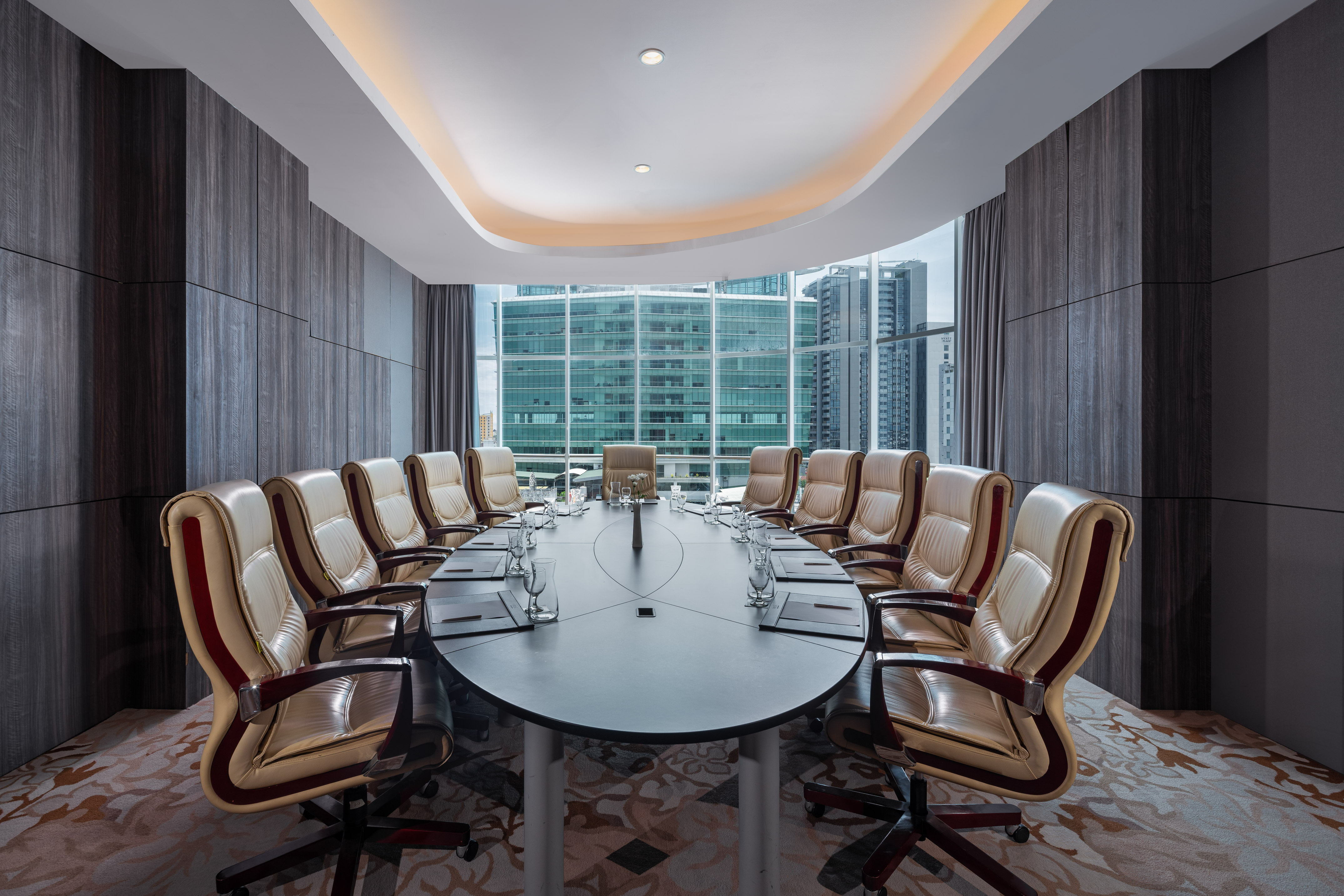 Modern conference room with oval table, leather chairs, and city skyline view.