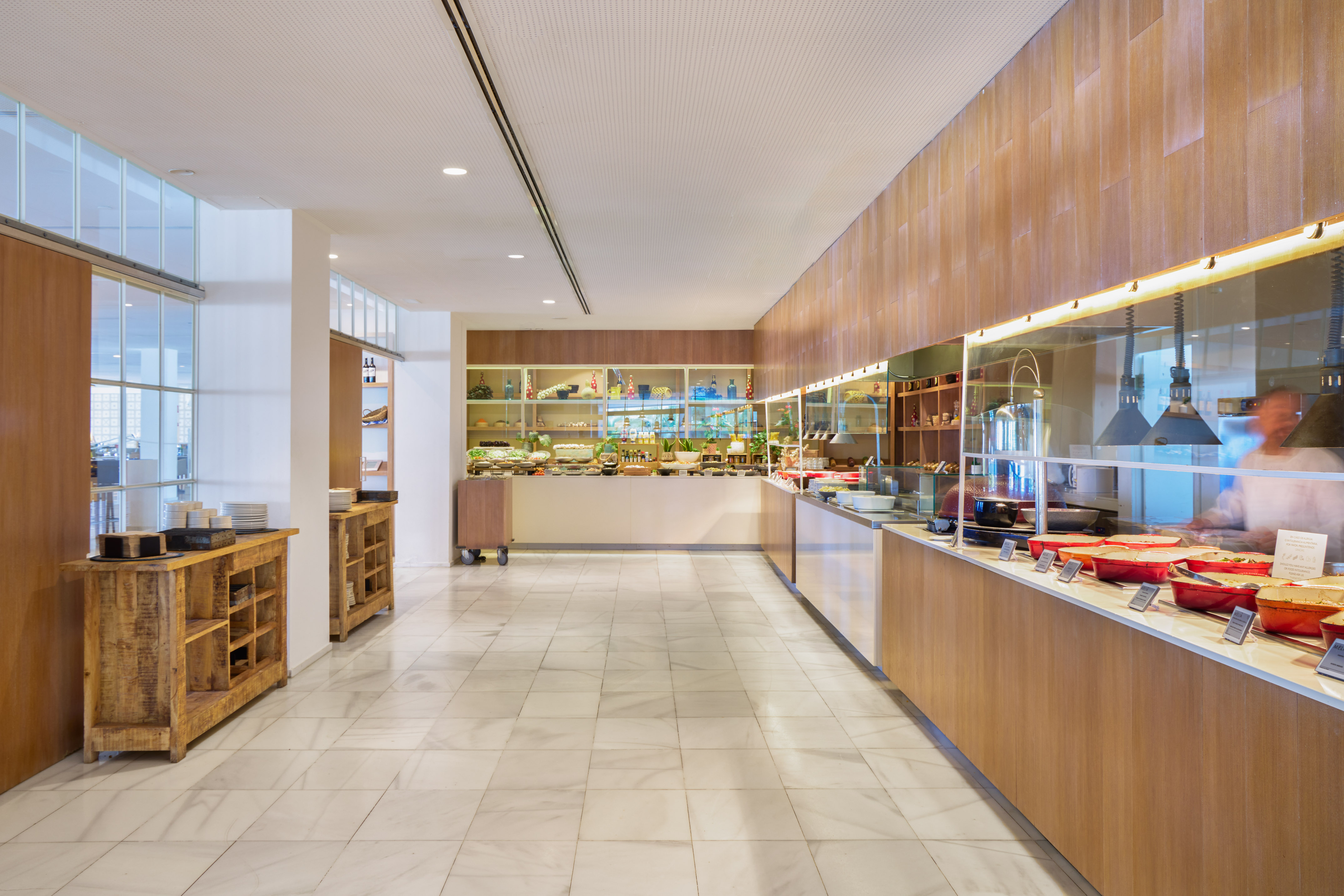 Modern hotel buffet with hot and cold food, marble floor, and wooden accents.