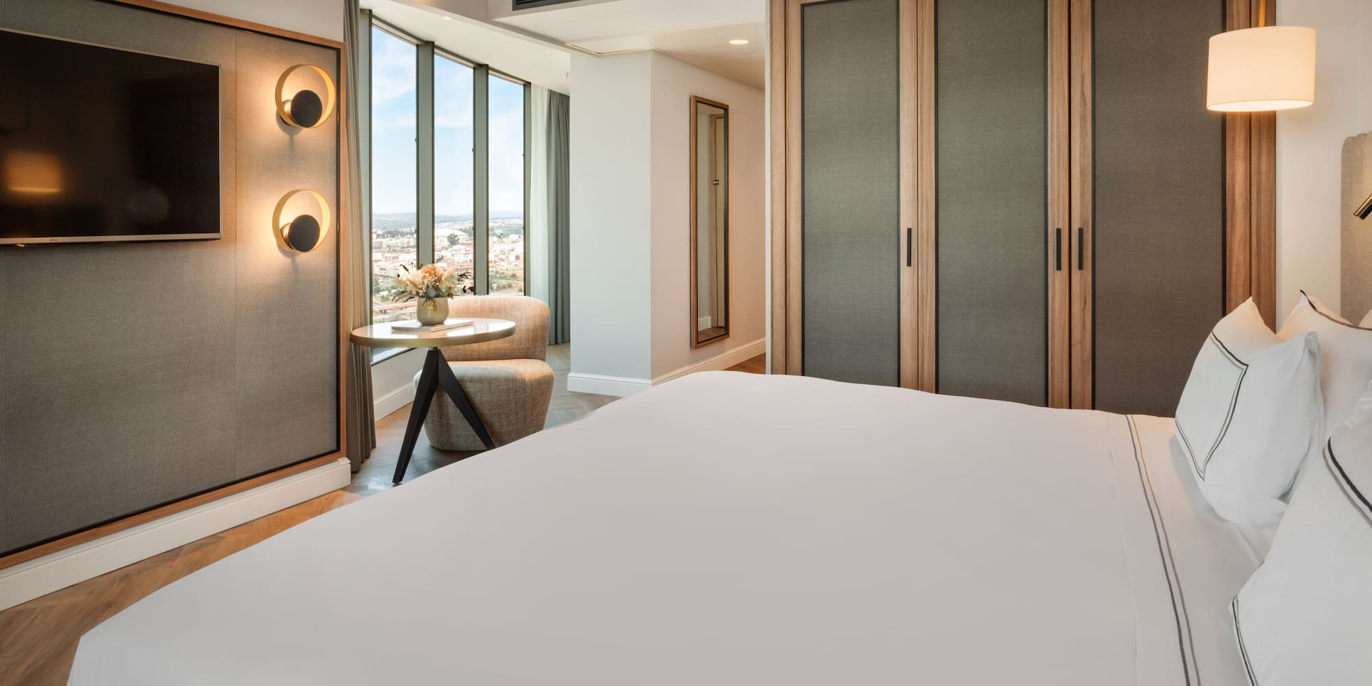 Habitación de hotel moderna con cama, TV, ventanales y vista a la ciudad.