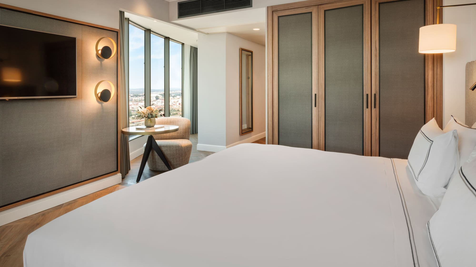 Habitación de hotel moderna con cama, TV, ventanales y vista a la ciudad.