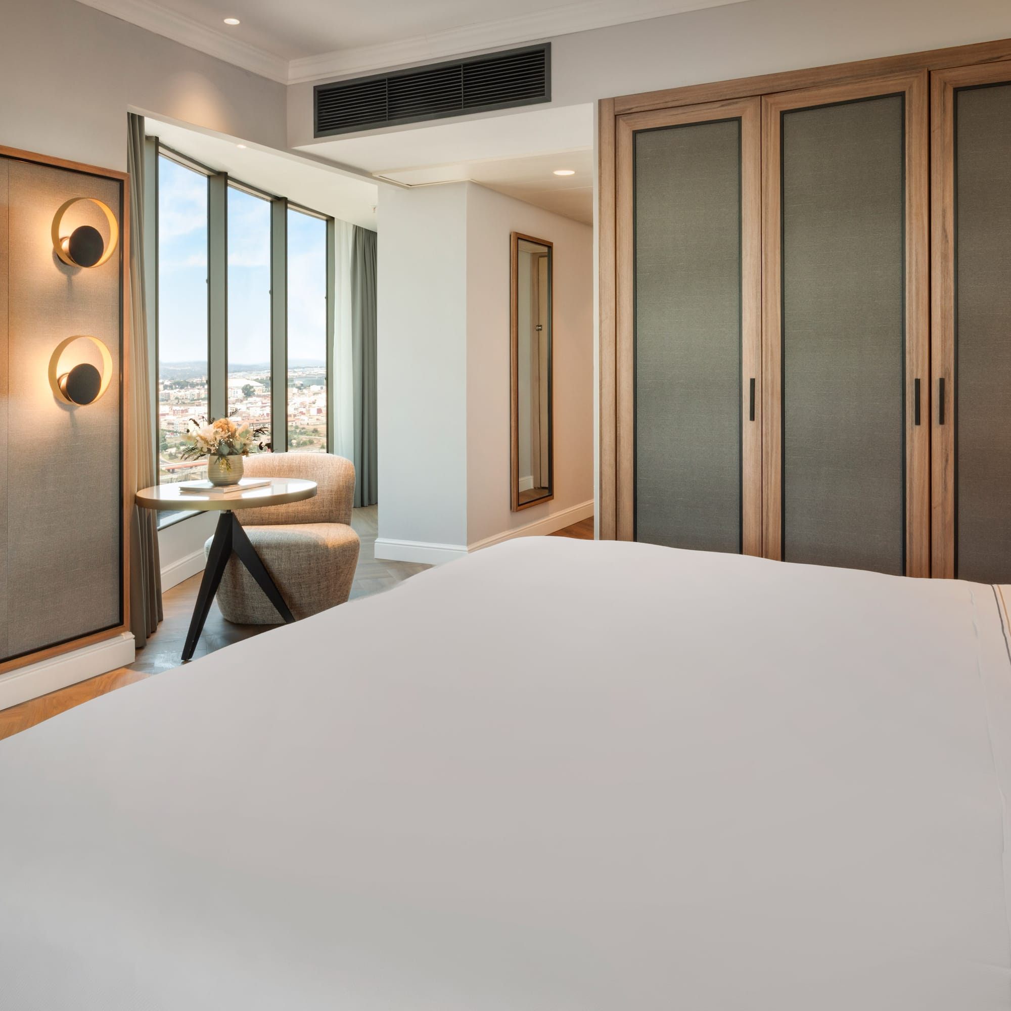 Habitación de hotel moderna con cama, TV, ventanales y vista a la ciudad.
