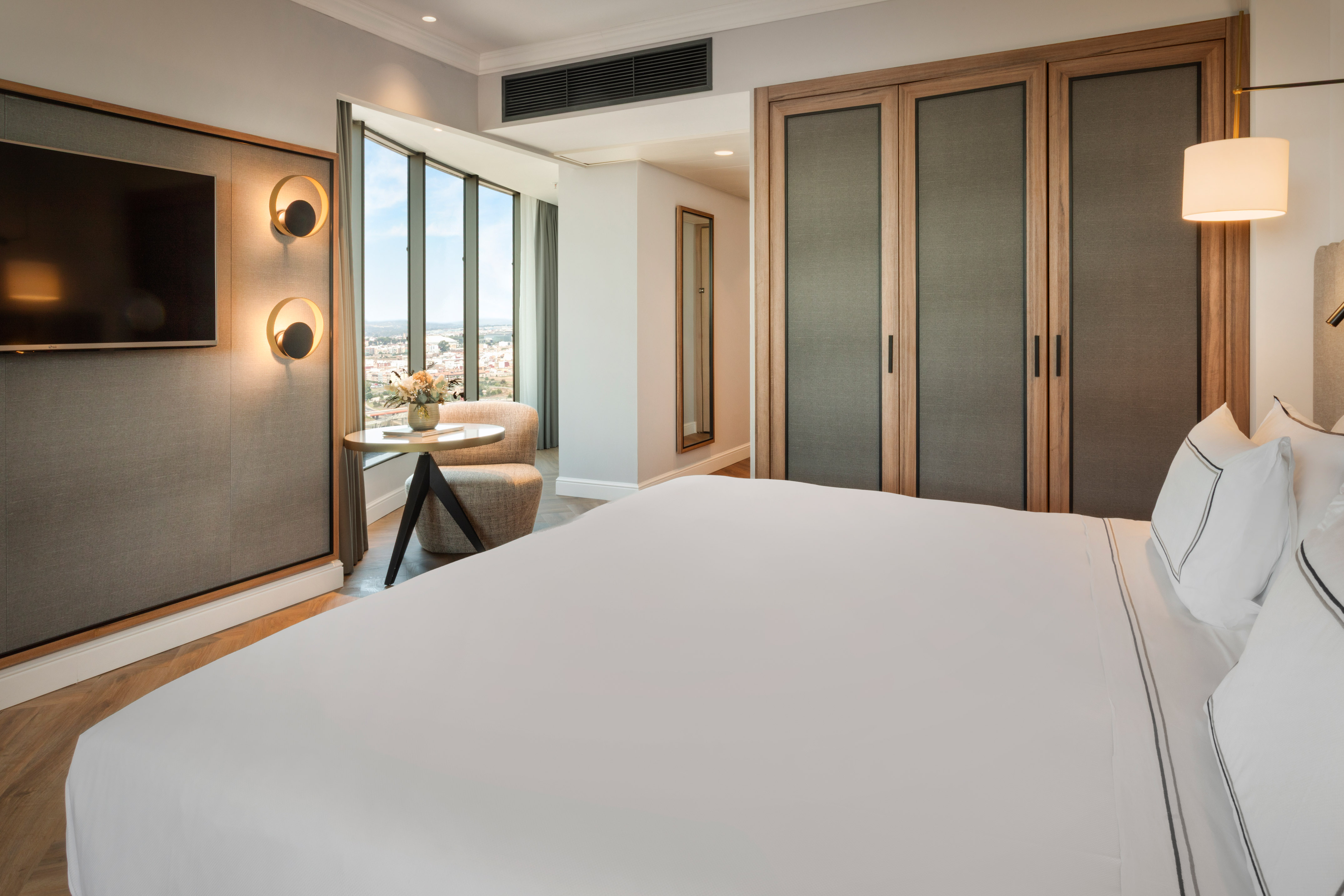 Habitación de hotel moderna con cama, TV, ventanales y vista a la ciudad.