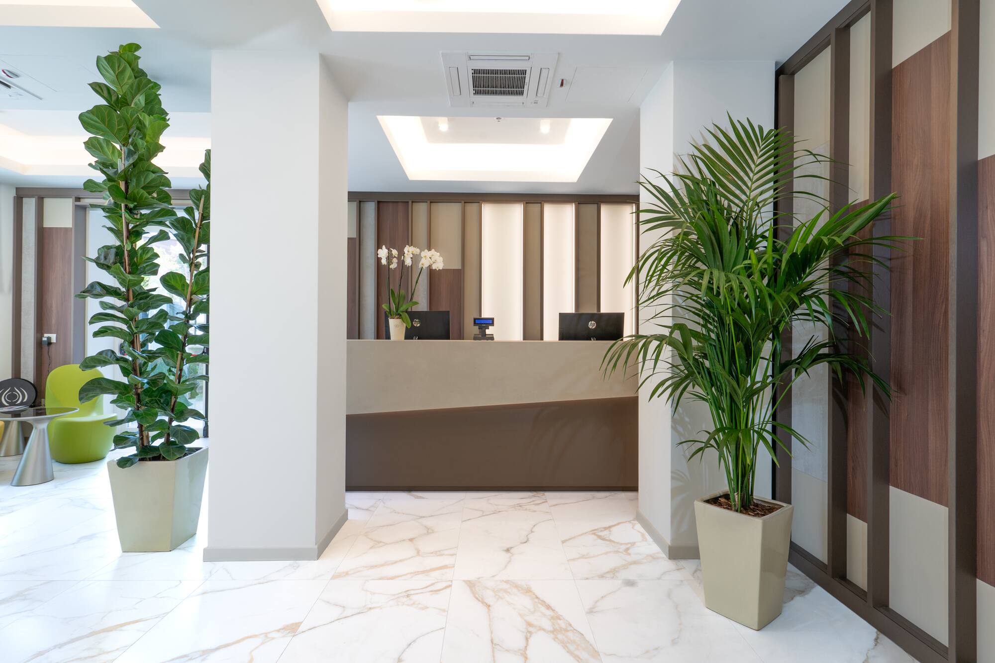 Bright hotel reception area with modern desk, marble floor, and lush greenery.