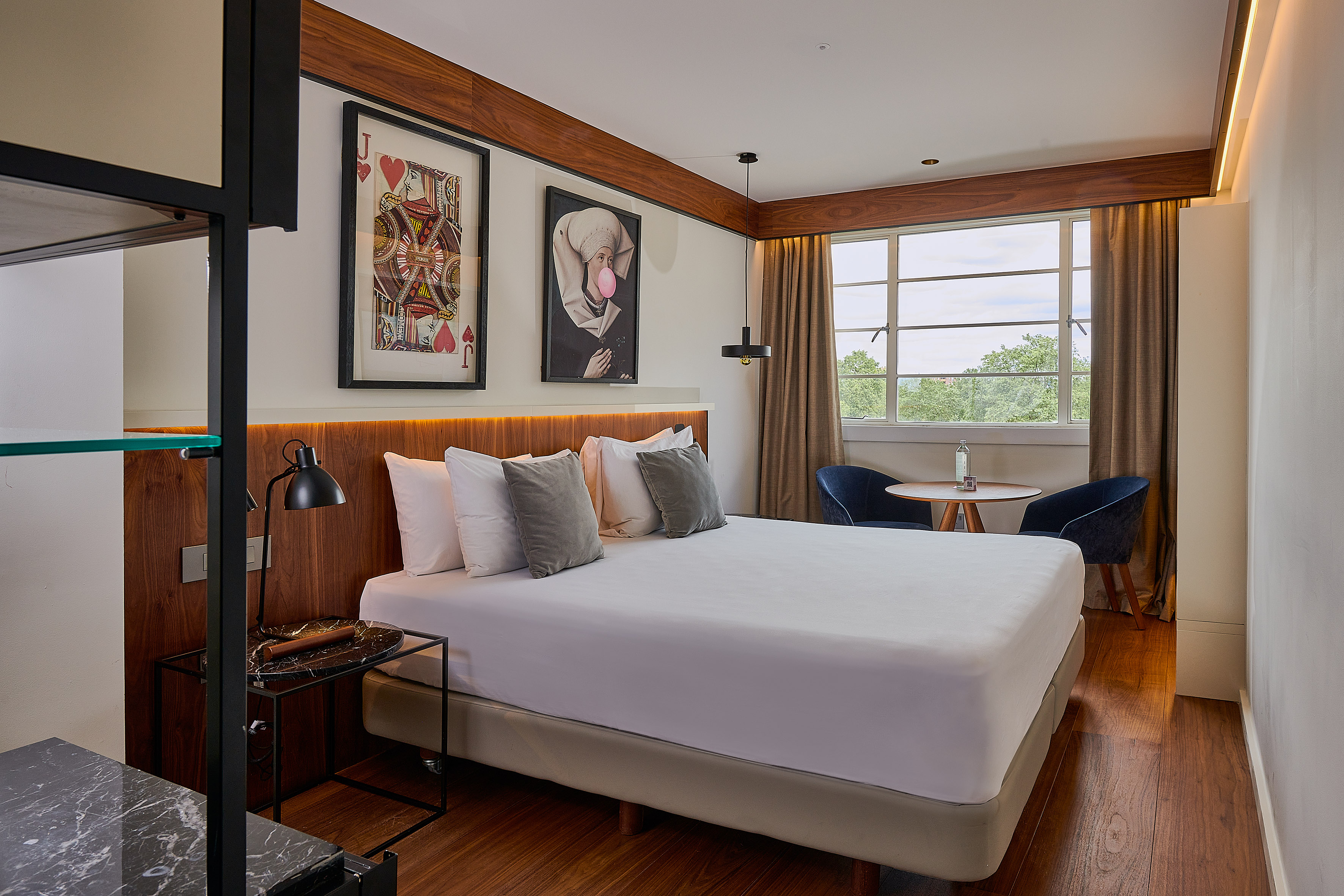 Chic hotel room featuring a king bed, hardwood, window view, and unique art.