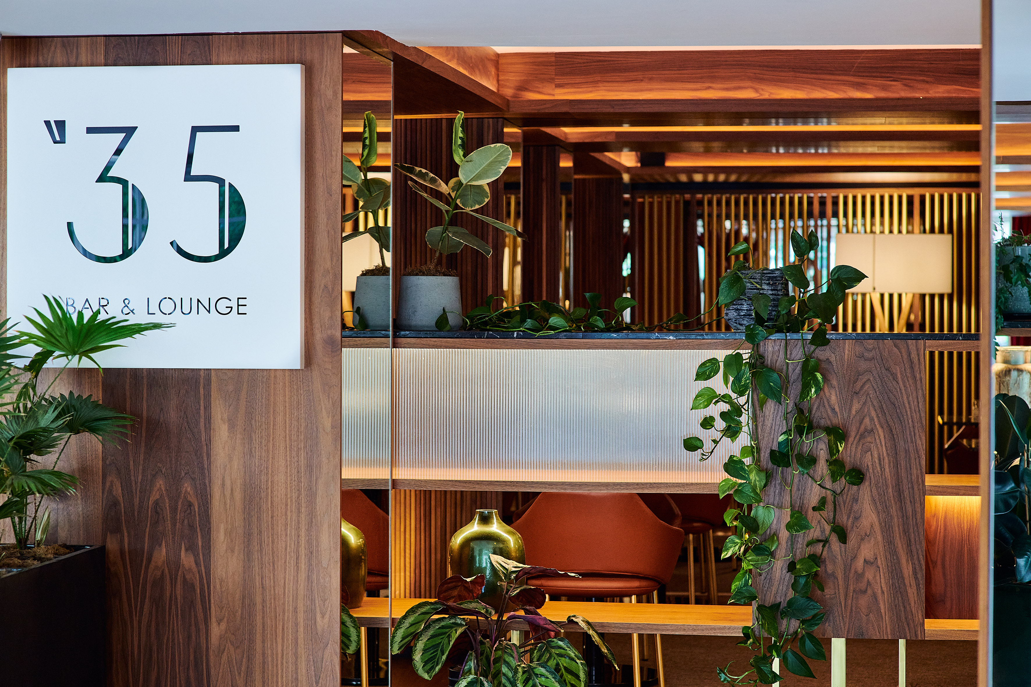 Modern '35 Bar & Lounge' sign, sleek wood paneling, and green interior plants.