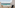 Tropical resort balcony overlooking turquoise ocean with chairs.