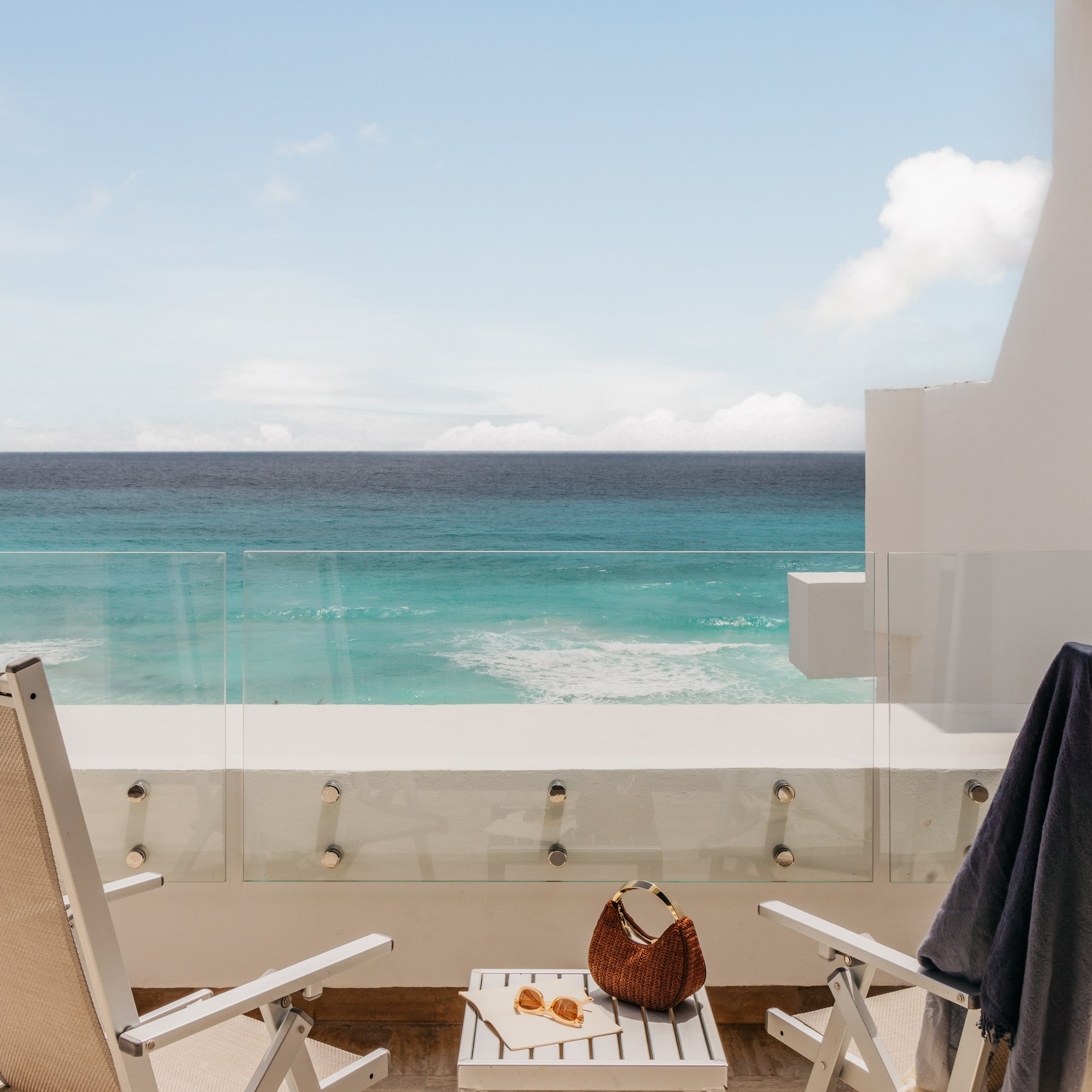 Tropical resort balcony overlooking turquoise ocean with chairs.