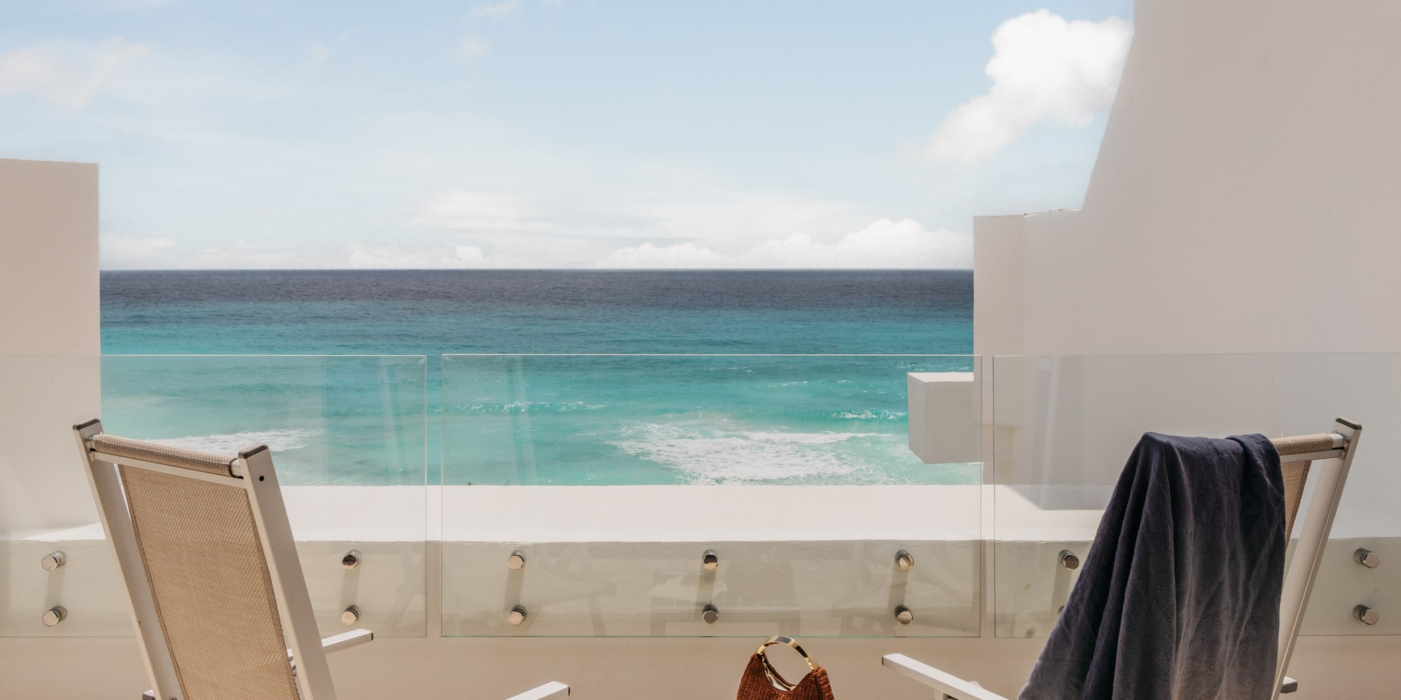 Tropical resort balcony overlooking turquoise ocean with chairs.