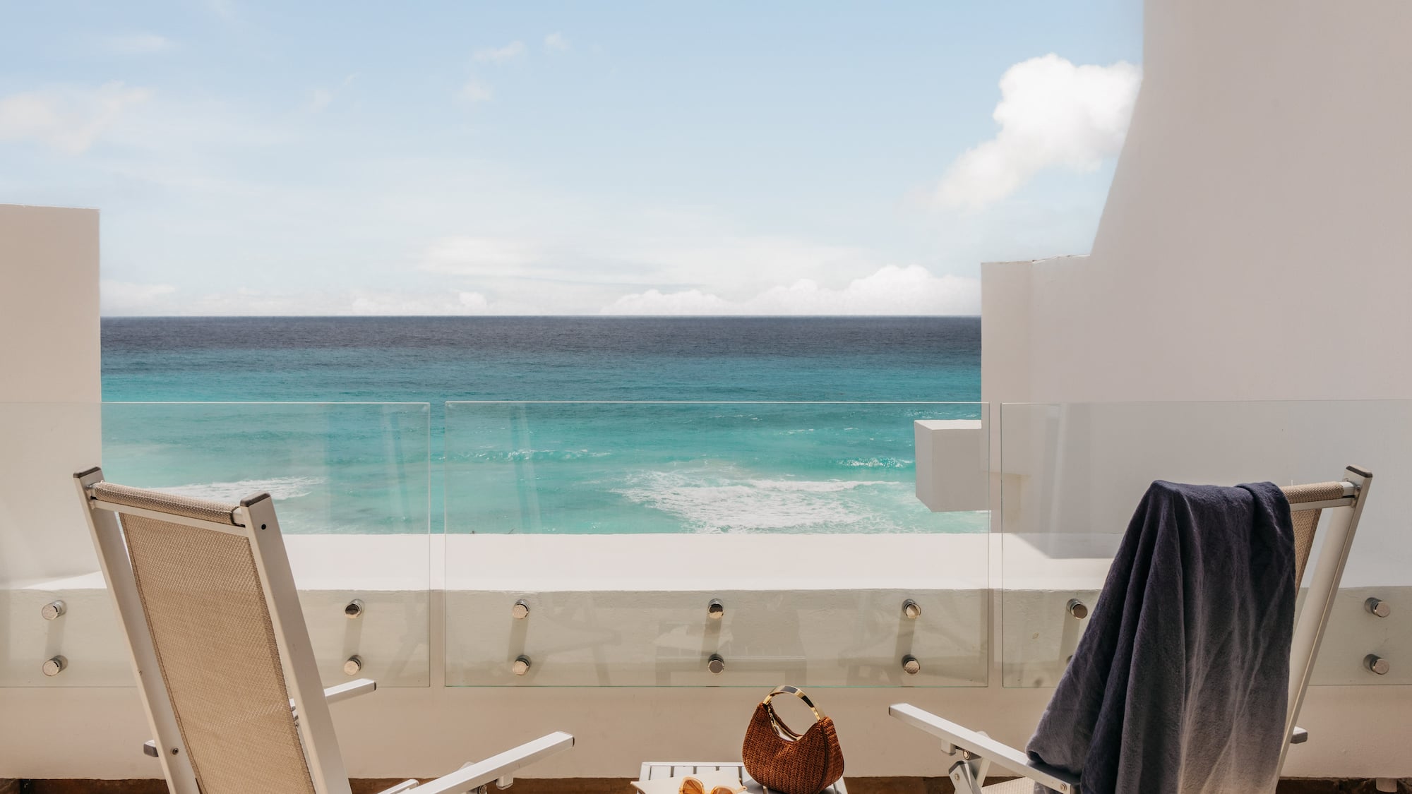 Tropical resort balcony overlooking turquoise ocean with chairs.