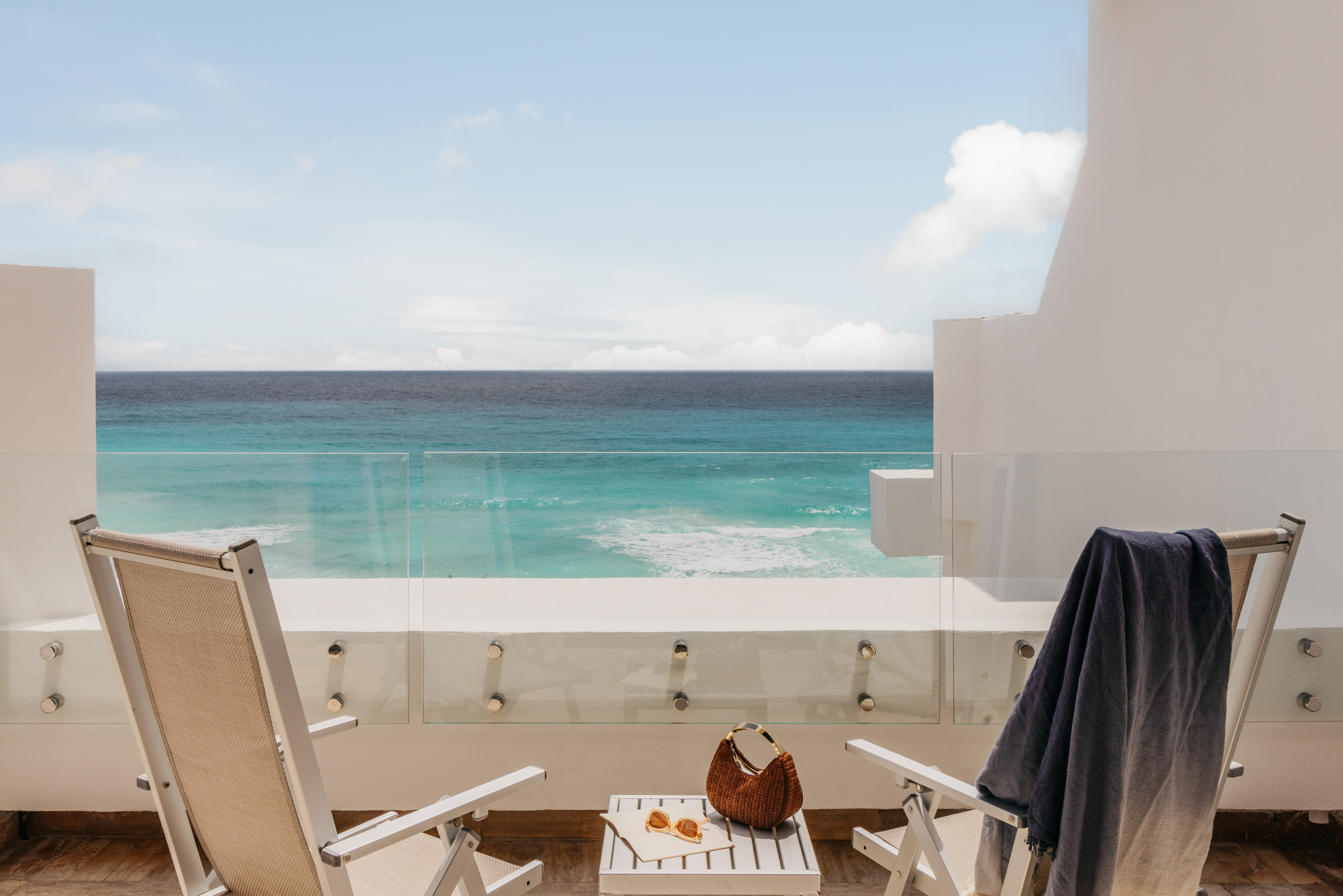 Tropical resort balcony overlooking turquoise ocean with chairs.