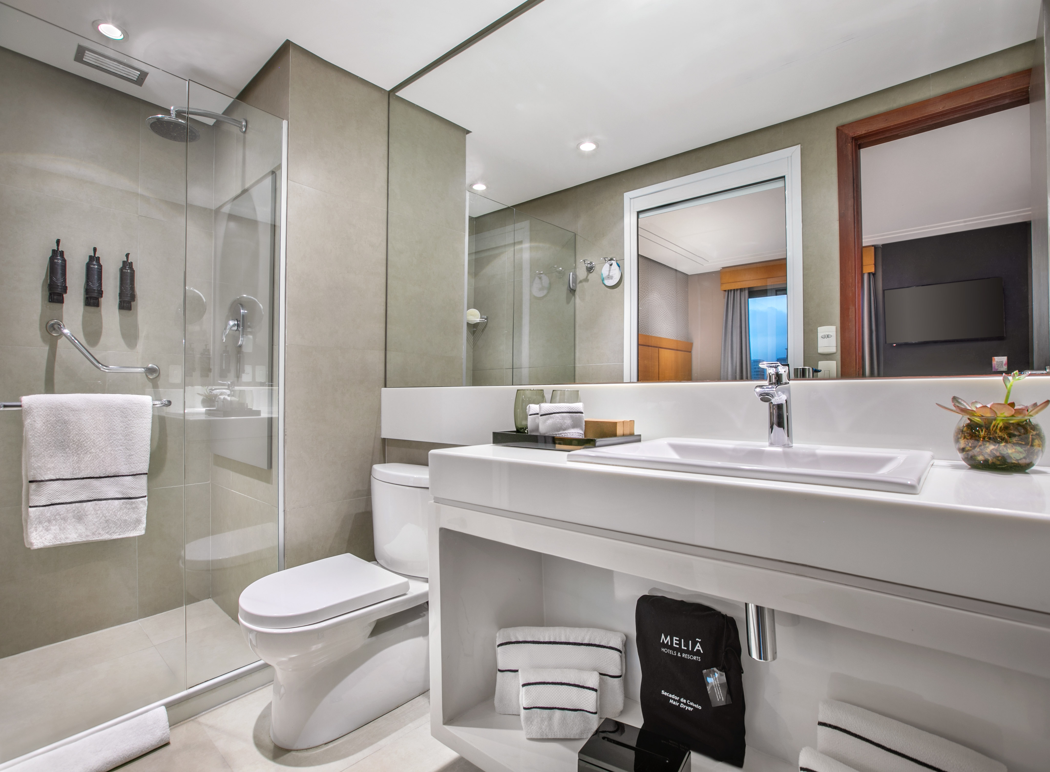 Modern Meliá hotel bathroom with glass shower, white vanity, sink, and toilet.