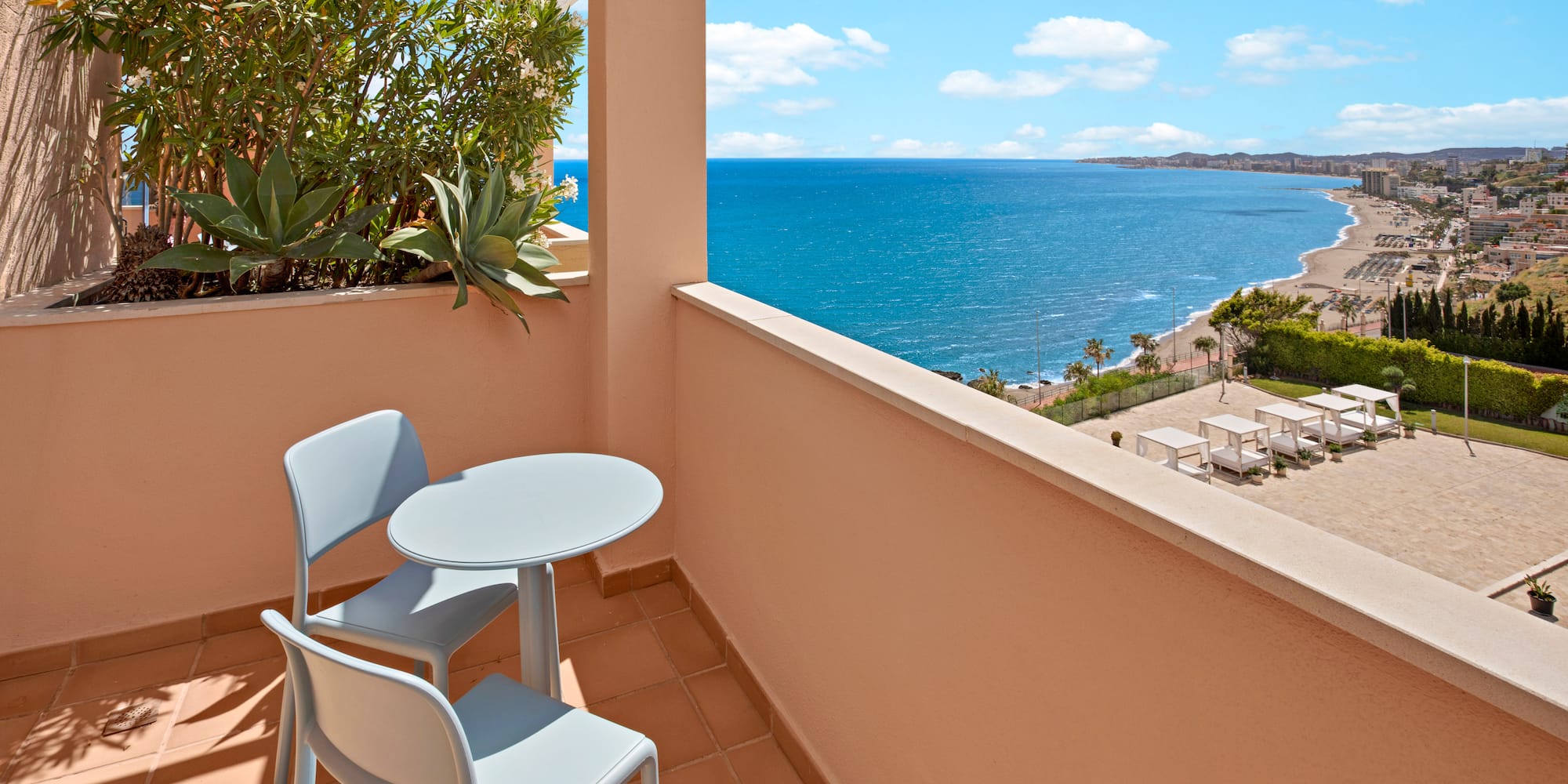 Resort balcony with table, chairs, and panoramic ocean view over beach.