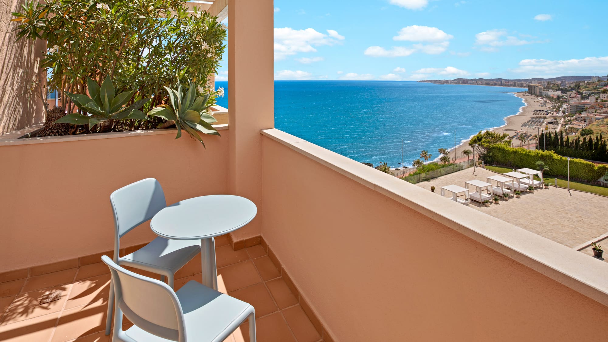 Resort balcony with table, chairs, and panoramic ocean view over beach.
