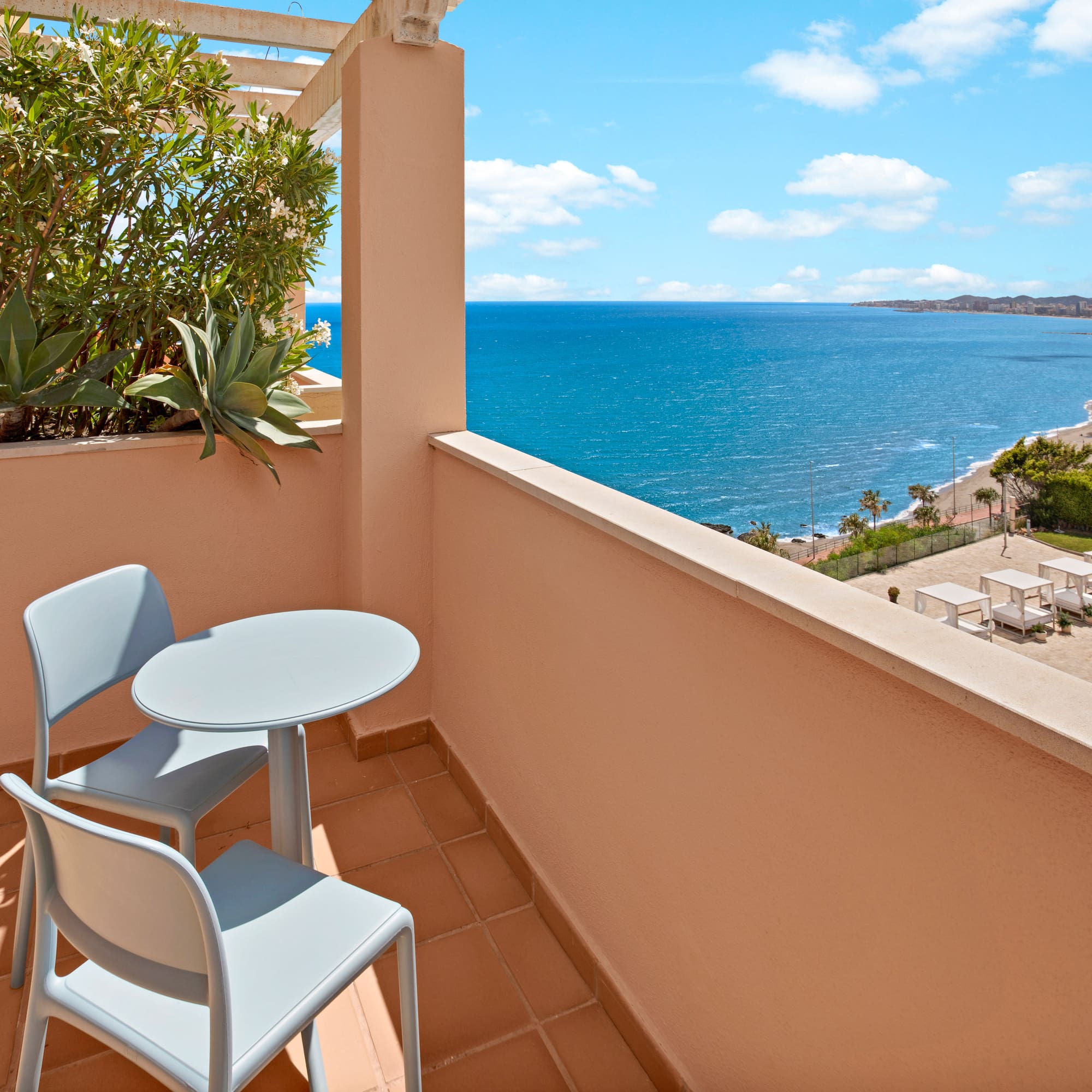 Resort balcony with table, chairs, and panoramic ocean view over beach.