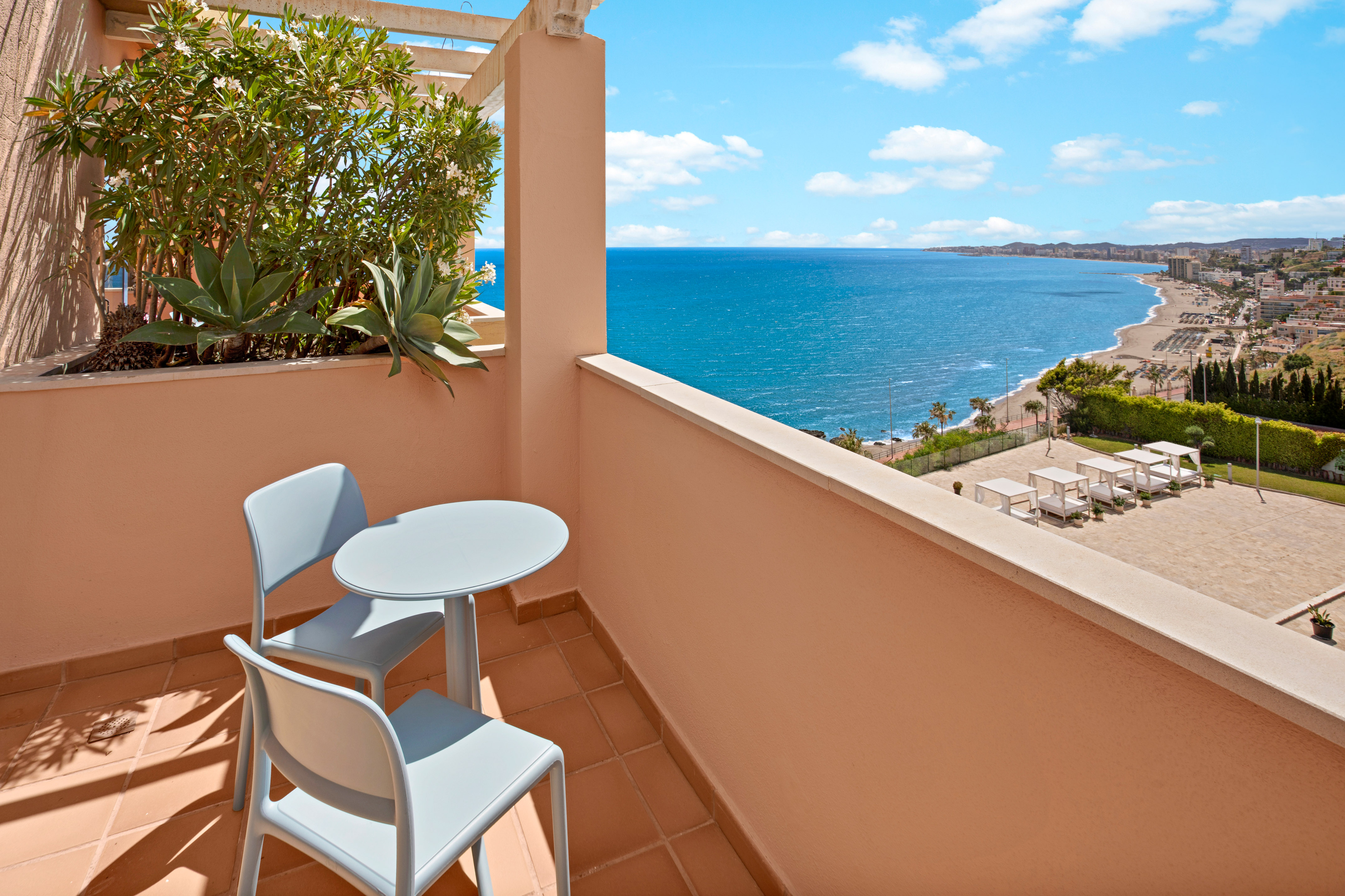 Resort balcony with table, chairs, and panoramic ocean view over beach.