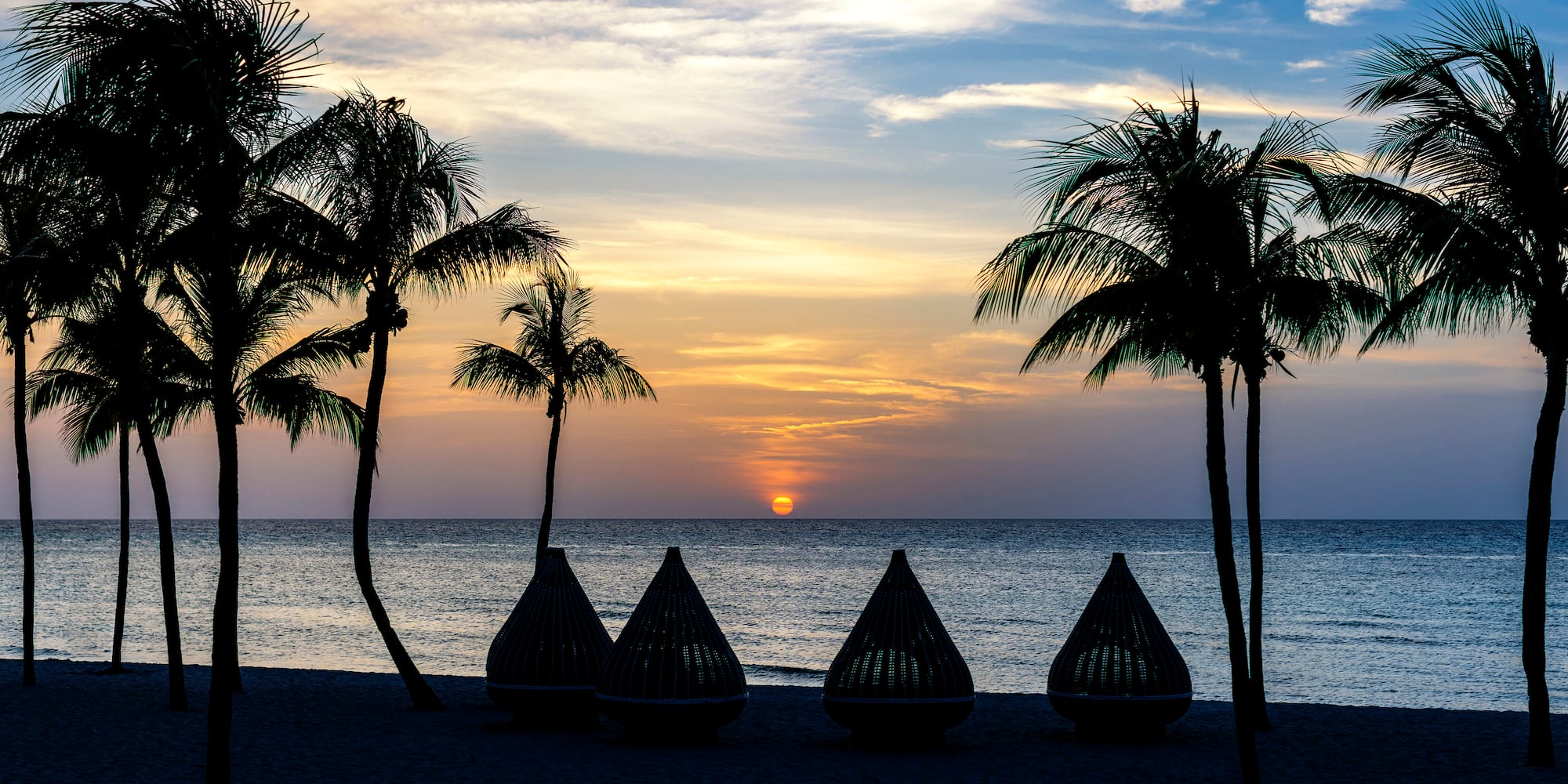a group of chairs on a beach with palm trees and a sunset