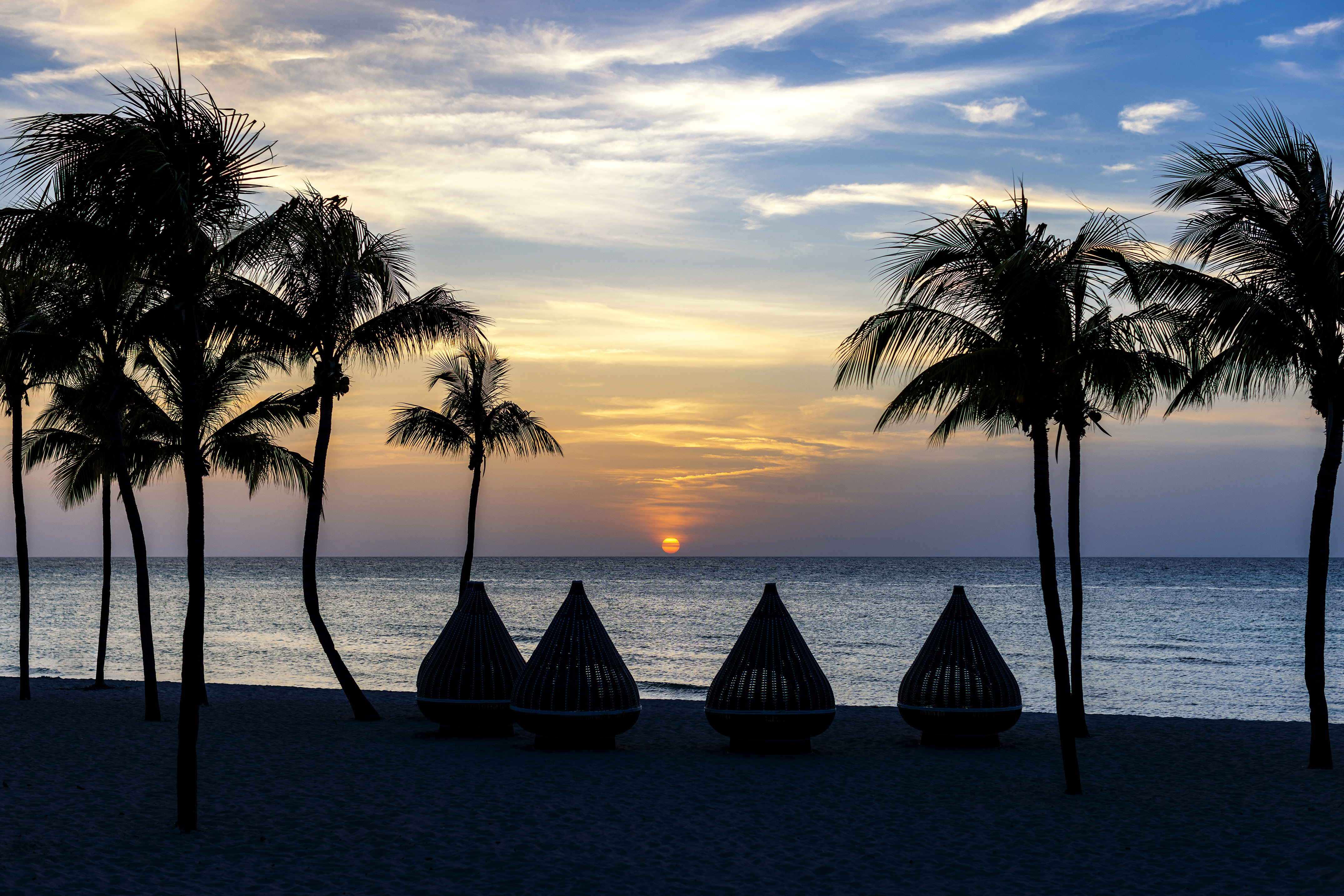a group of chairs on a beach with palm trees and a sunset